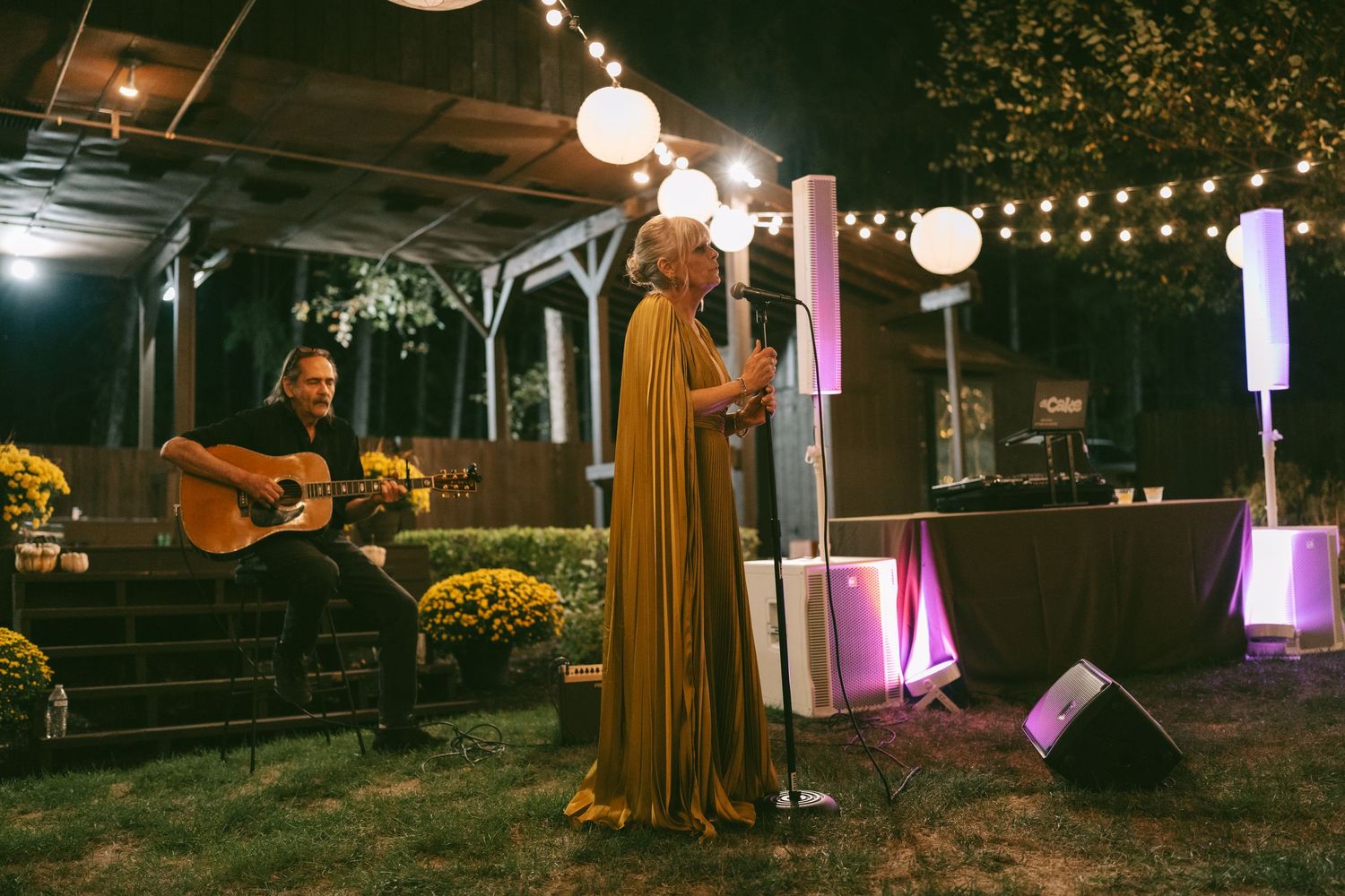String lights and lanterns illuminate an outdoor nighttime event space with purple accent lighting.