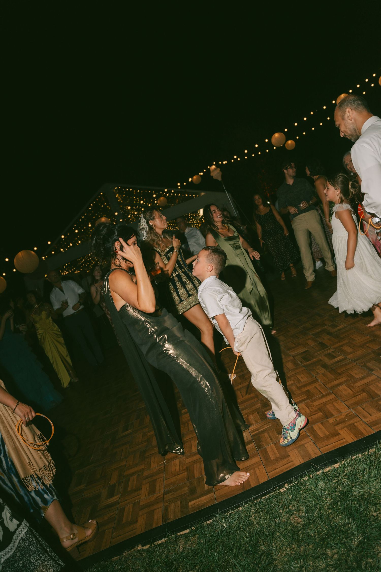 Wedding reception dance floor with guests dancing under string lights at night.