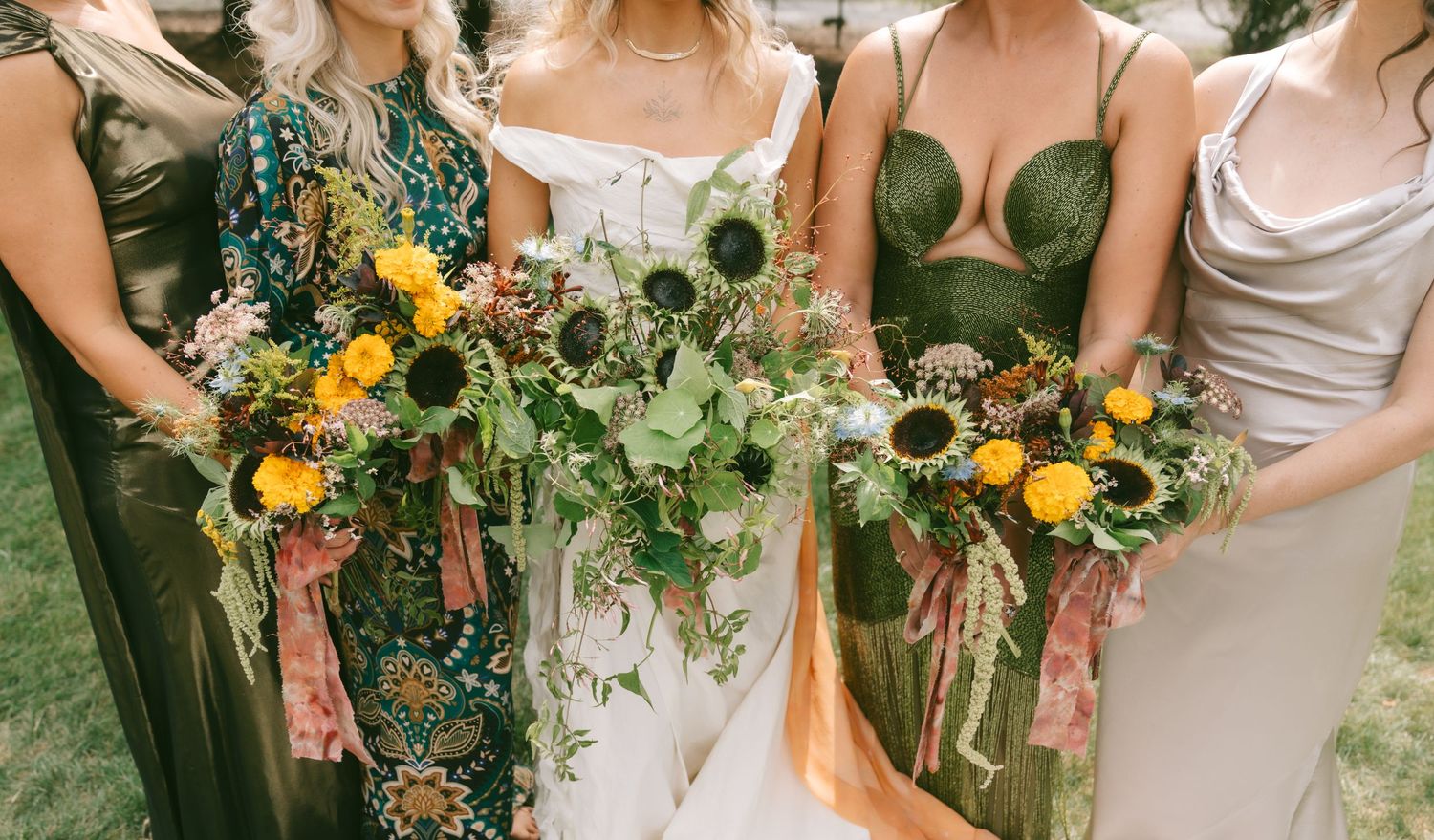 A wedding party holds vibrant sunflower and greenery bouquets while standing together outdoors.