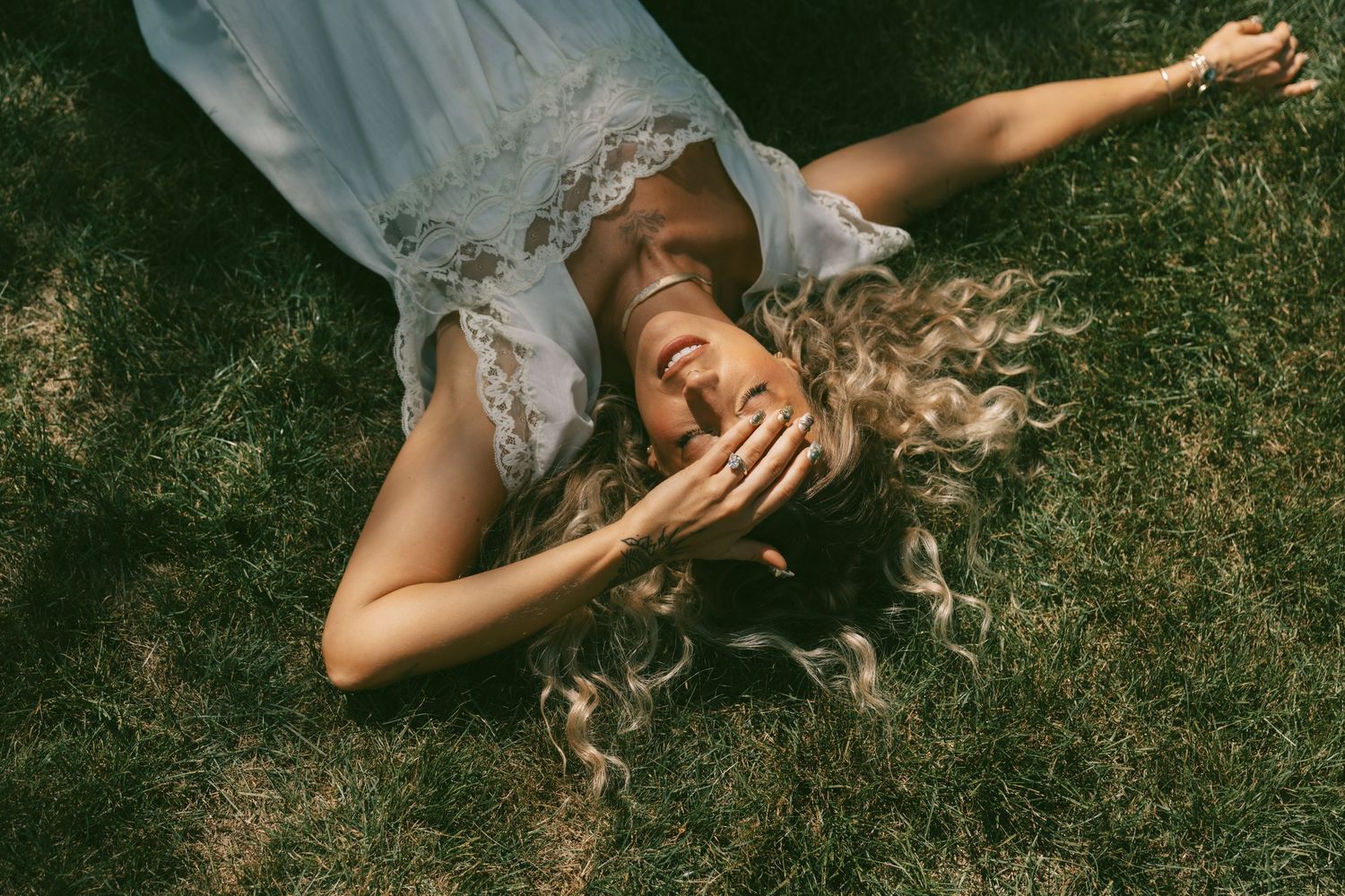 Someone lying in grass wearing a white dress with hair spread out.