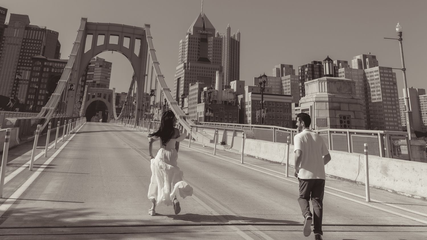 couple running on the Roberto Clemente Bridge in Pittsburgh with the downtown skyline in black and white in north shore.