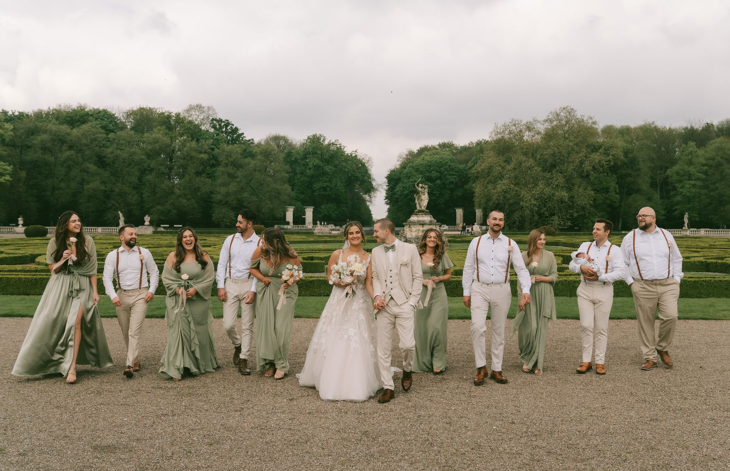 Wedding party in sage green and cream attire poses for formal photo on garden grounds in Germany.