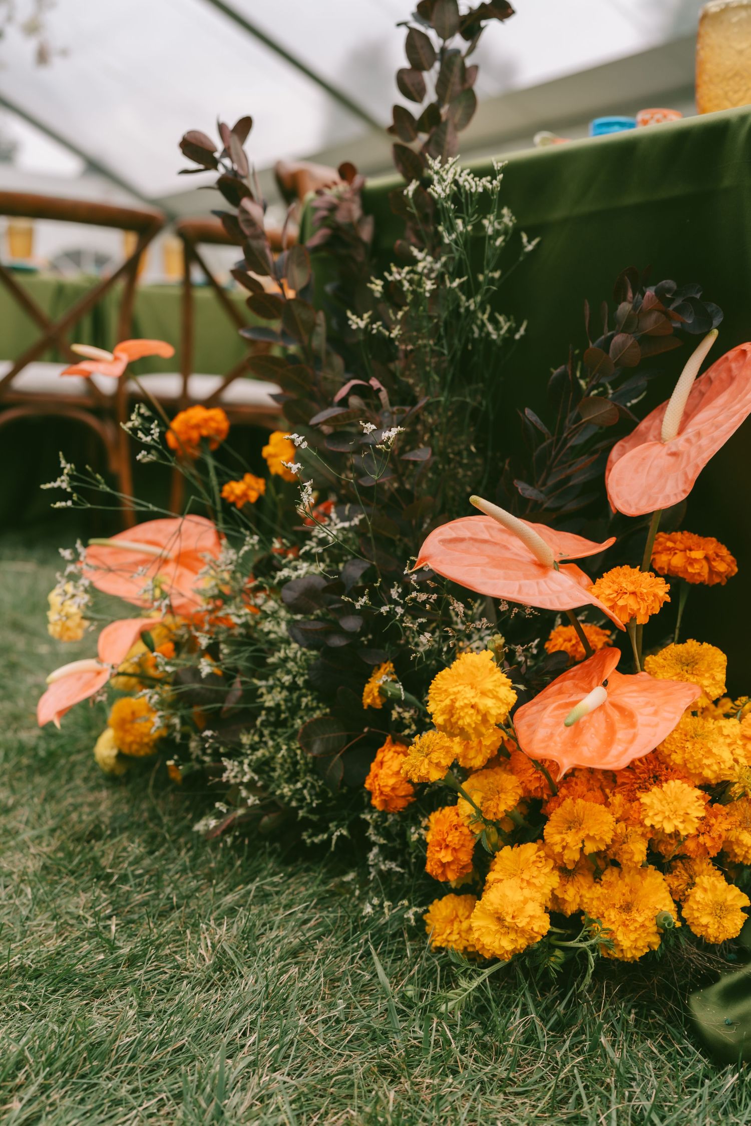 Orange marigolds and coral anthurium flowers arranged on green grass for wedding decor.