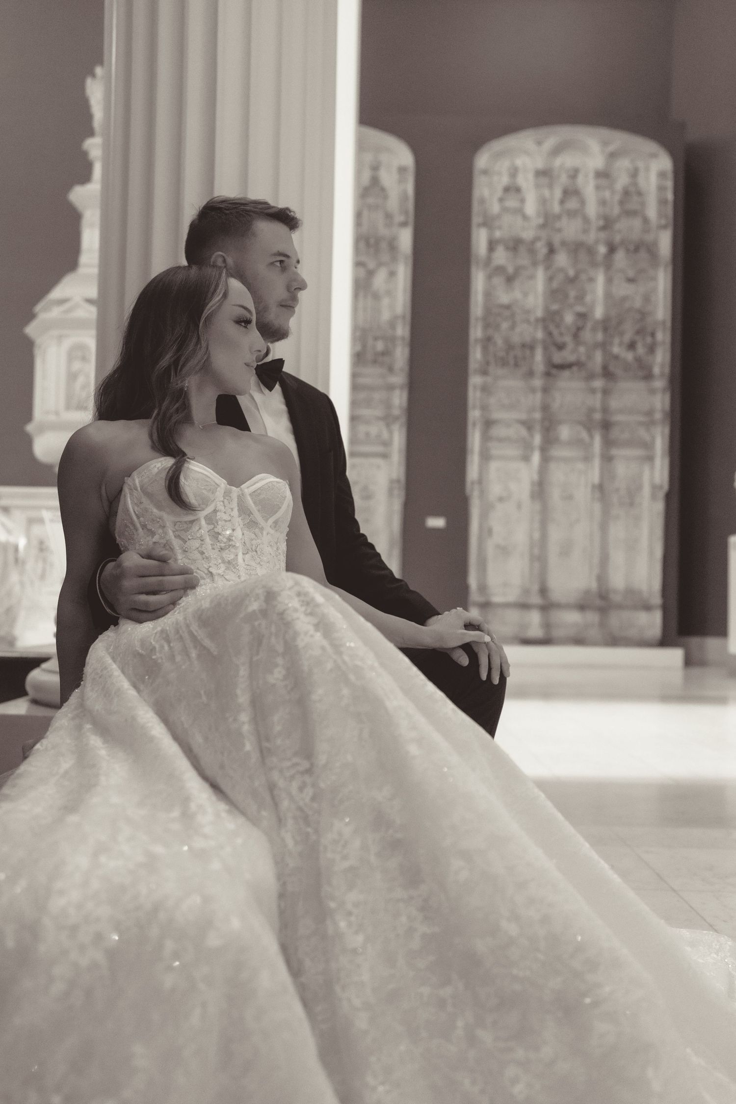 Elegant wedding couple embraces in a historic church corridor with ornate Gothic architecture and stained glass windows.