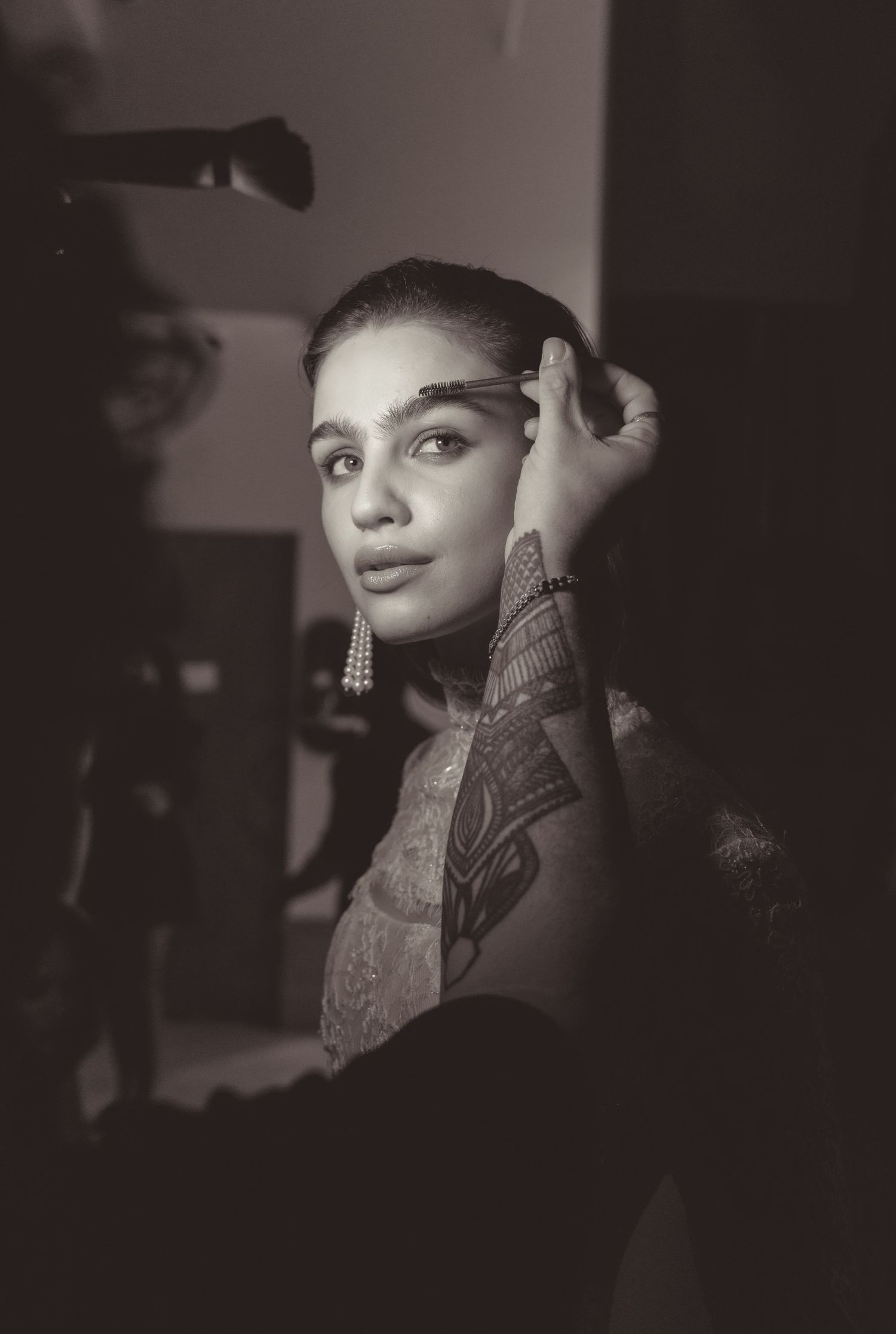 A black and white portrait photograph showing an elegant figure wearing dangling earrings and a patterned outfit.
