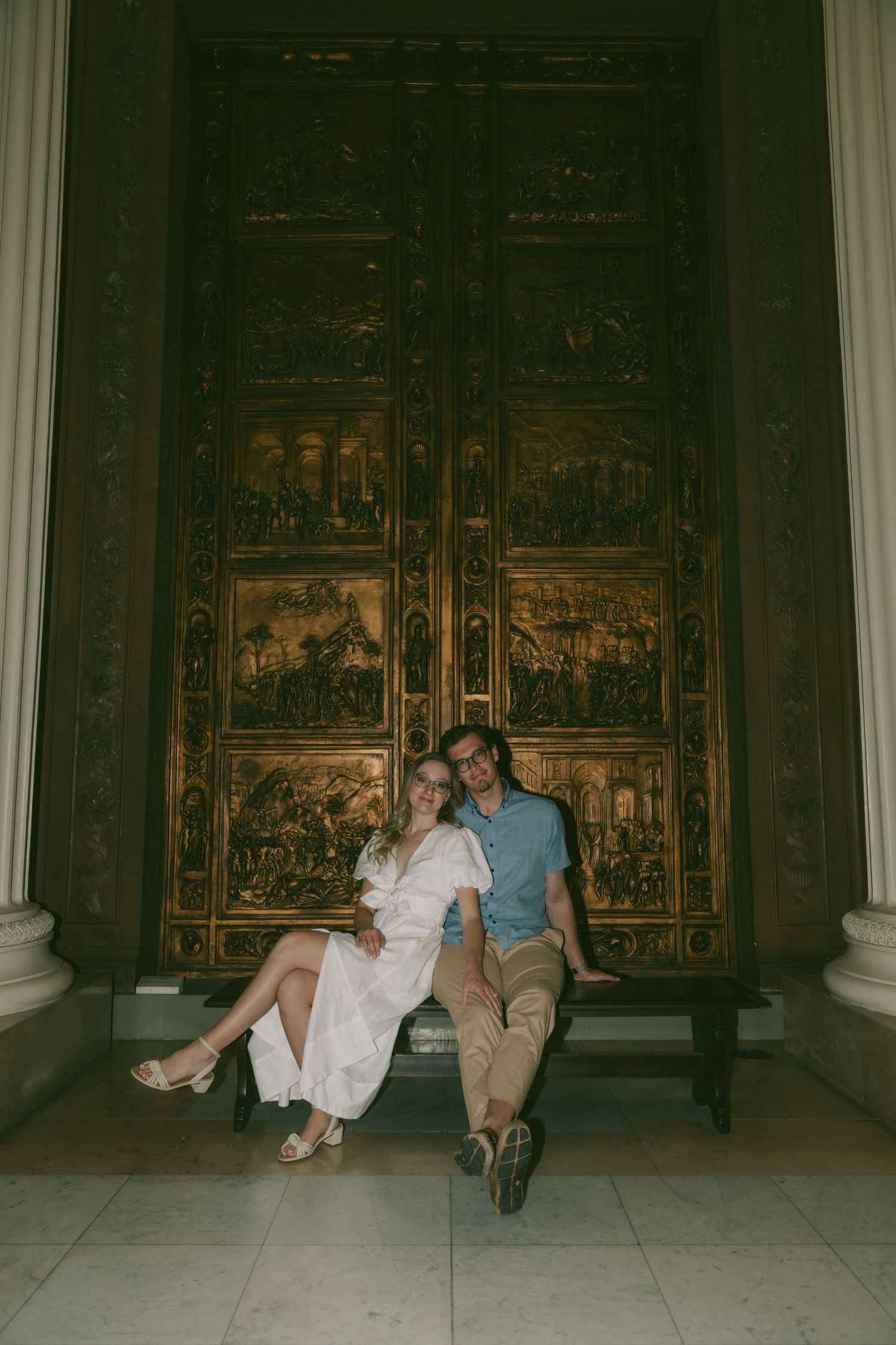 A couple sitting on the floor in front of an ornate altar or decorative wall panel.