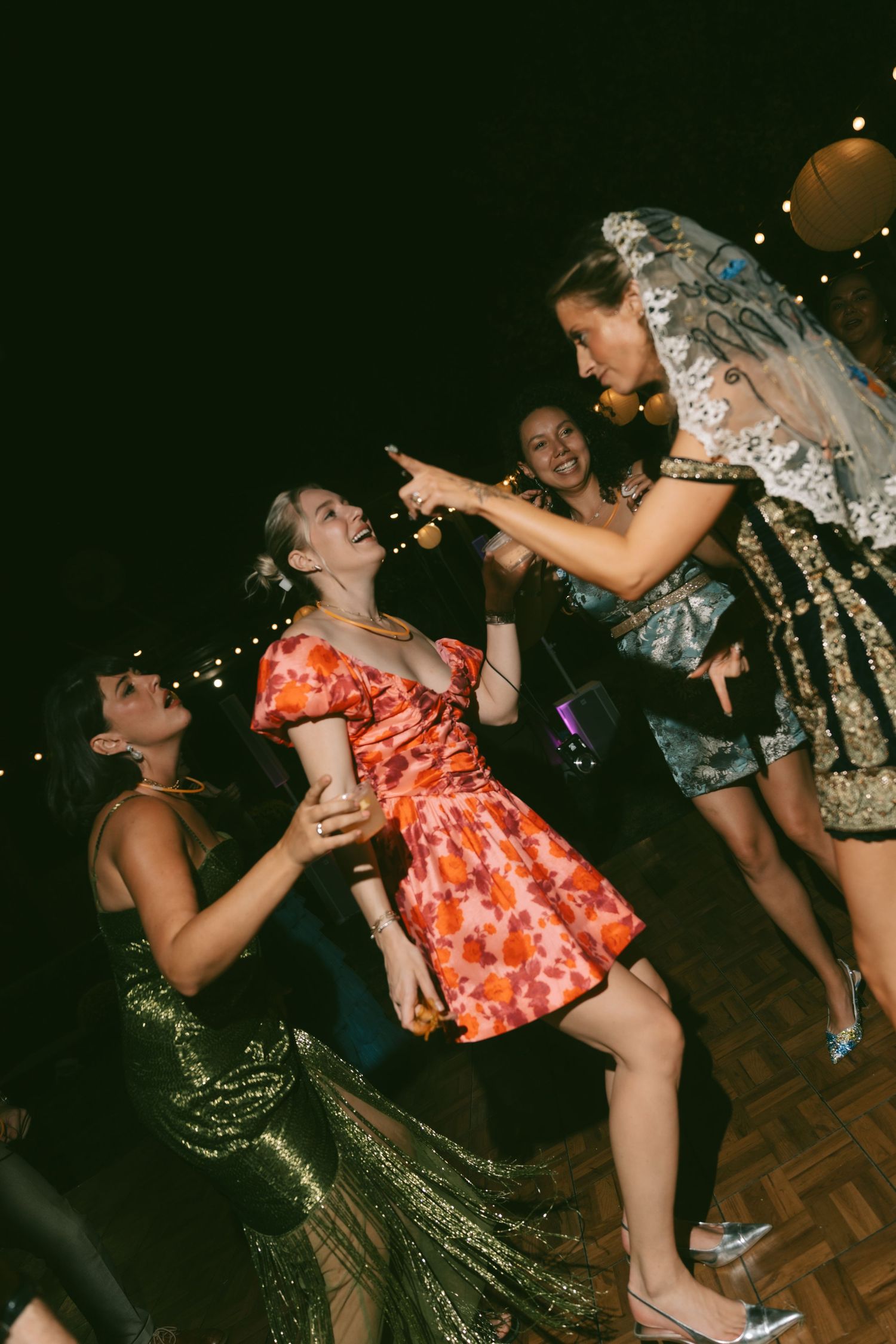 Party guests dance energetically on a wooden dance floor at night during festive celebration.
