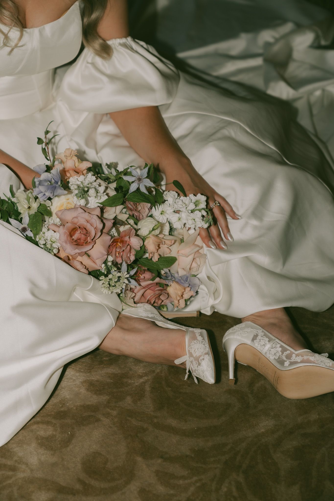 Delicate pink roses and white flowers rest on flowing white fabric against a moody dark brown background.