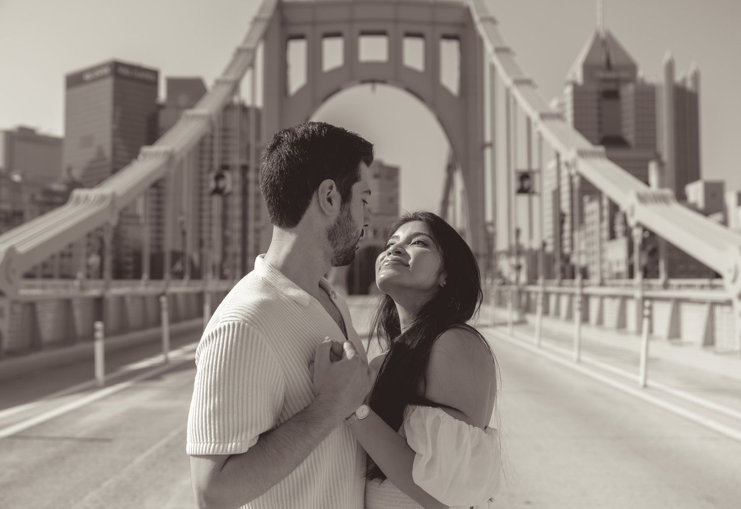 A romantic moment shared on a bridge with a city skyline in the background.