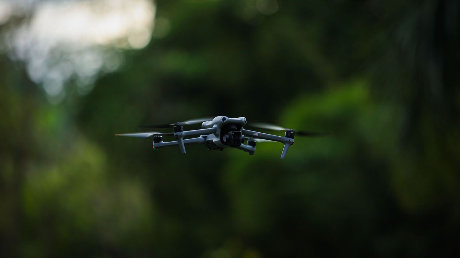 DJI drone hovering in mid-air against blurred green forest background during outdoor flight.
