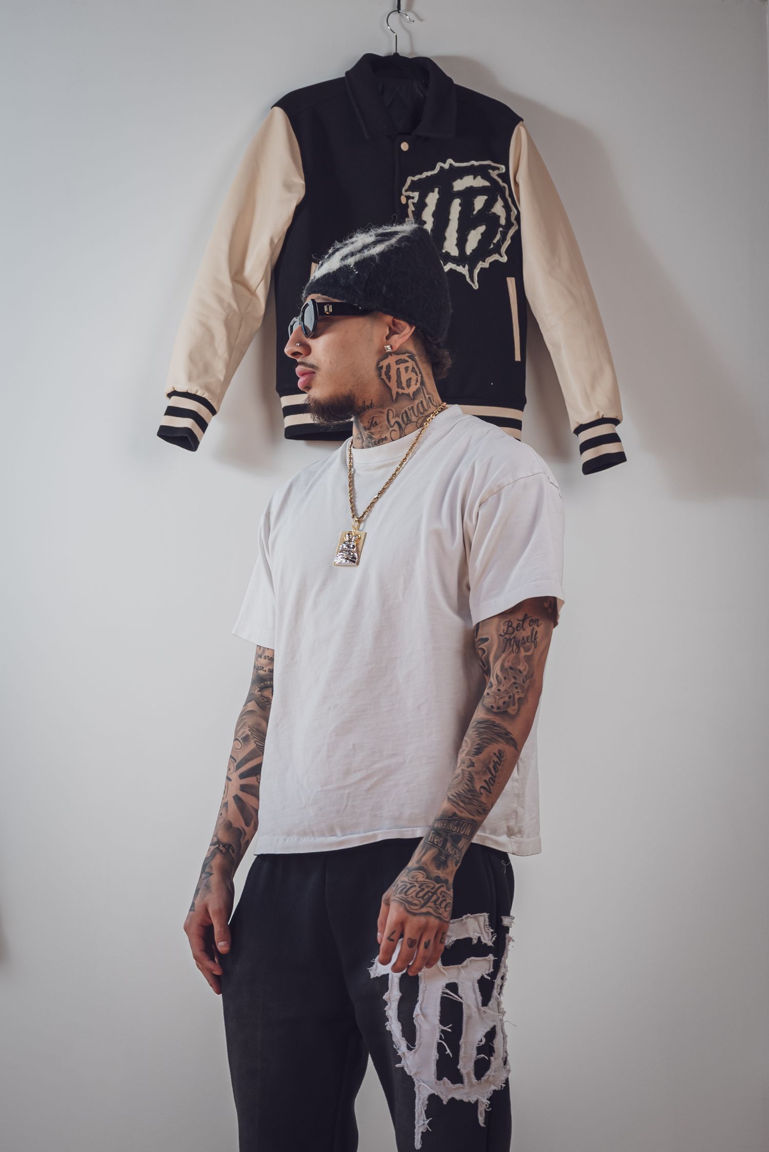 A heavily tattooed person wearing a white t-shirt poses next to a varsity jacket on display. goose.img photography LLC  Chicago Photographer