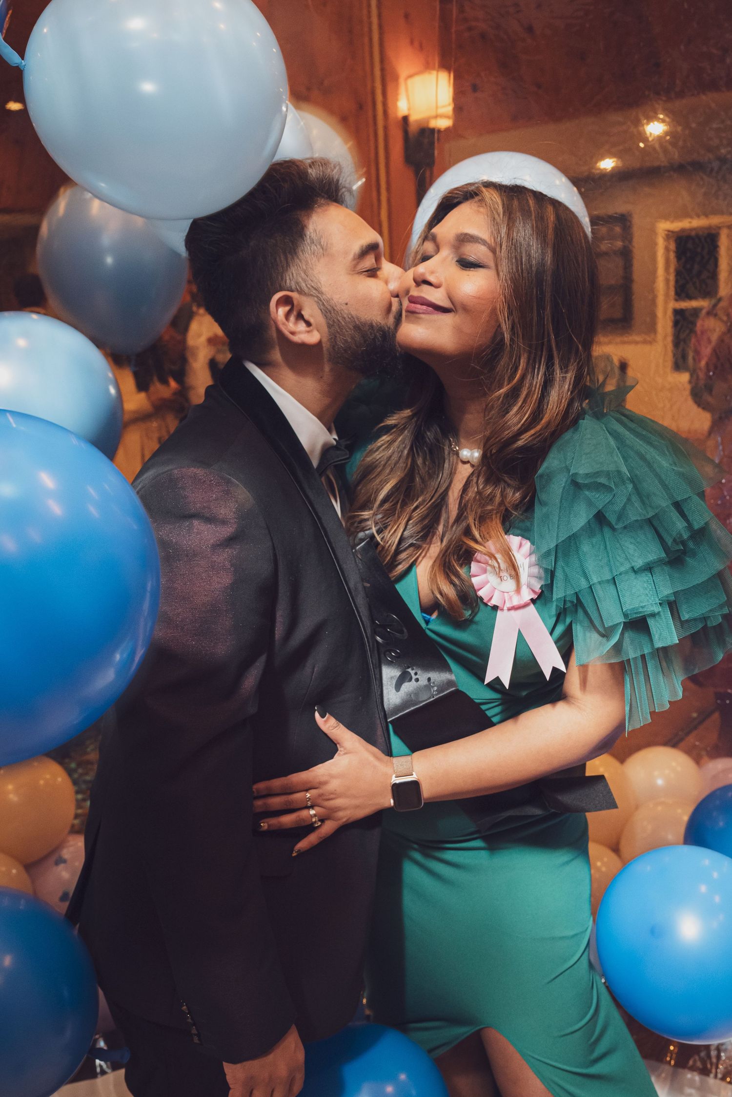 A couple sharing an intimate moment surrounded by blue and gold balloons at a celebration. goose.img photography LLC - Chicago Photographer