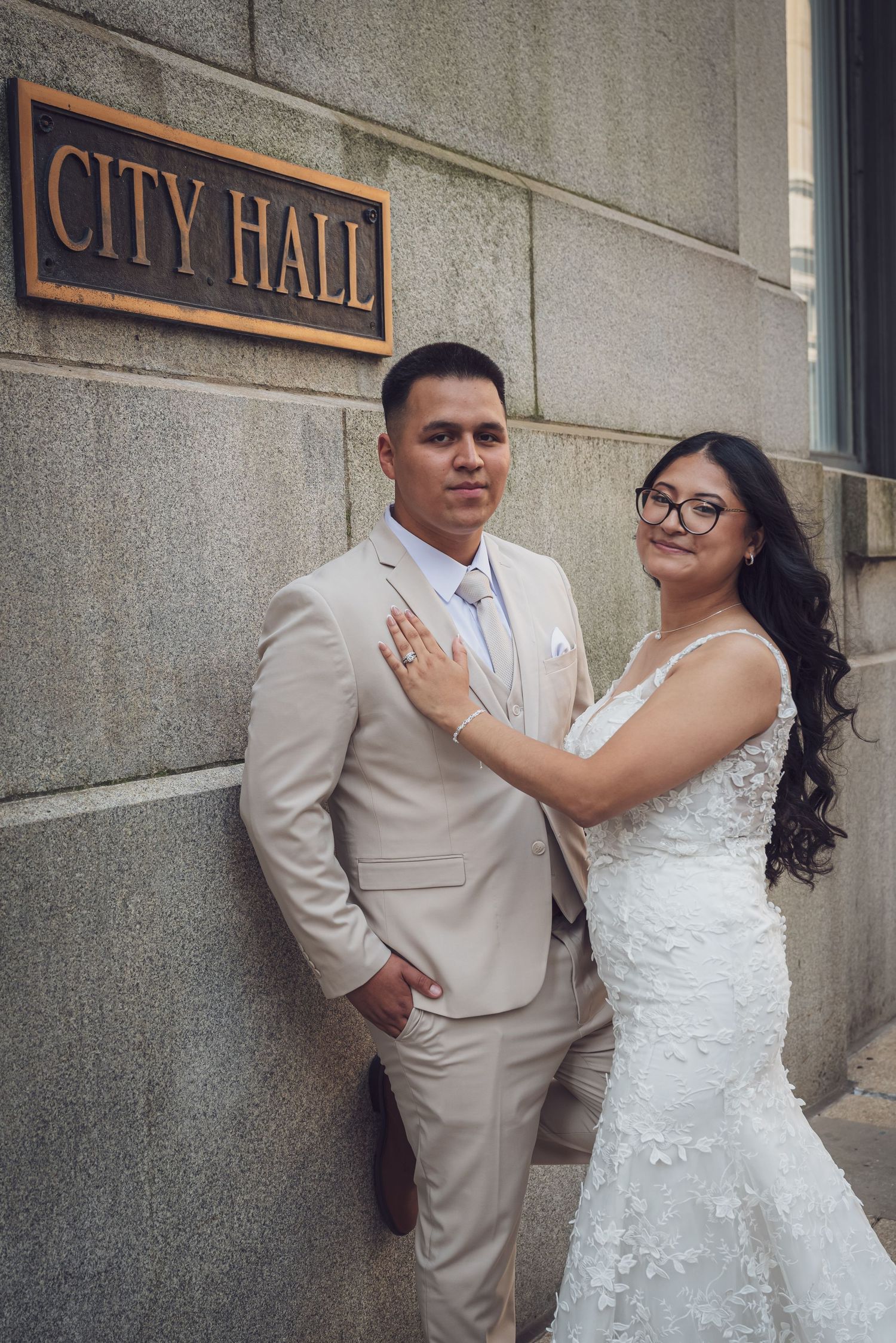 A couple in wedding attire poses together outside a city hall building in a romantic series of photos.