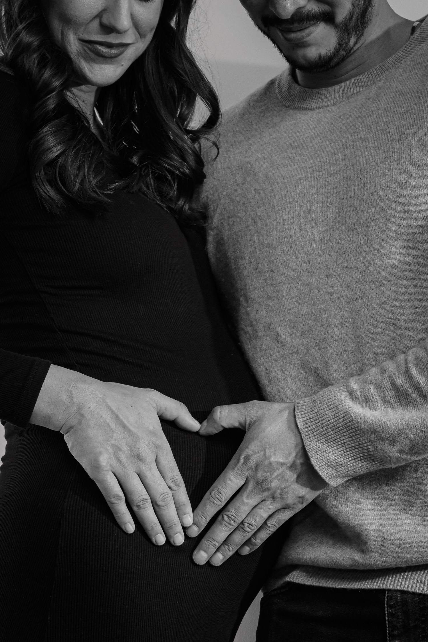 A black and white close-up of hands forming a heart shape over a pregnant belly. goose.img photography LLC - Chicago Photographer