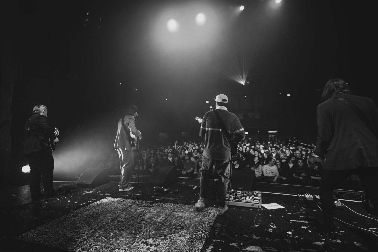 A black and white panoramic collage of concert performance scenes with stage lighting and crowd silhouettes.