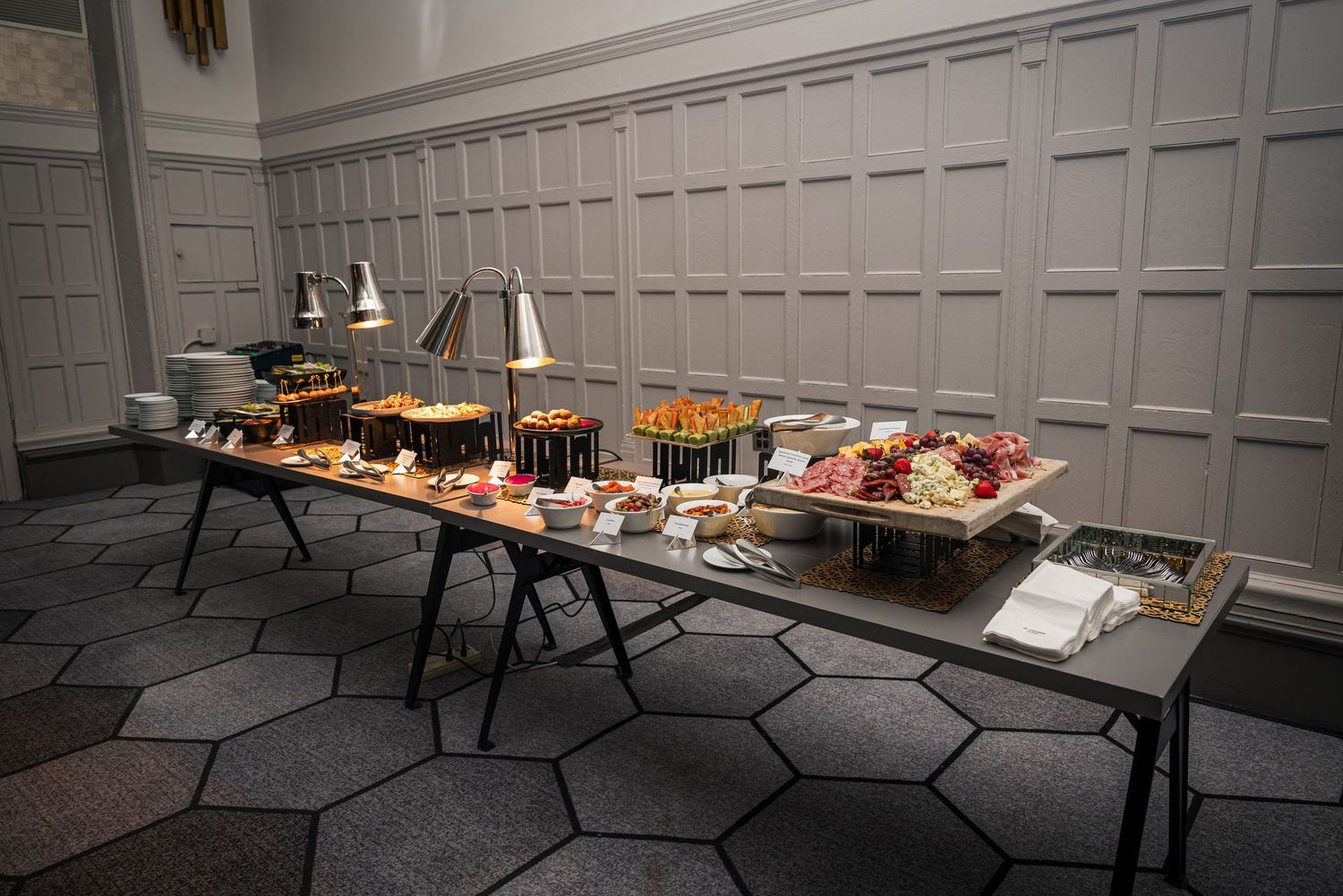 A long buffet table with various appetizers and catering dishes displayed on black tables against a gray paneled wall.