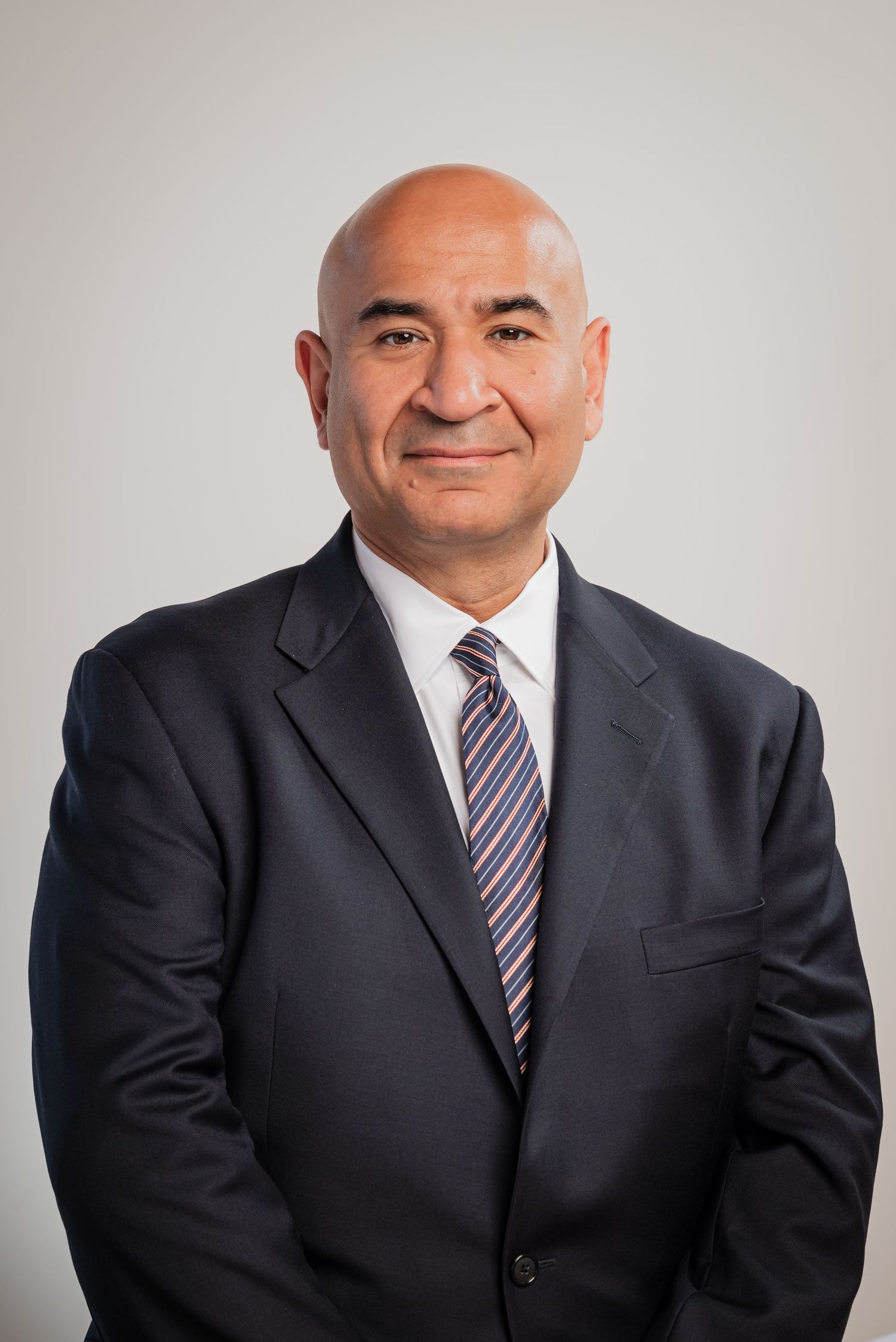 Professional headshot series showing a person in a dark suit and striped tie against a light gray background.