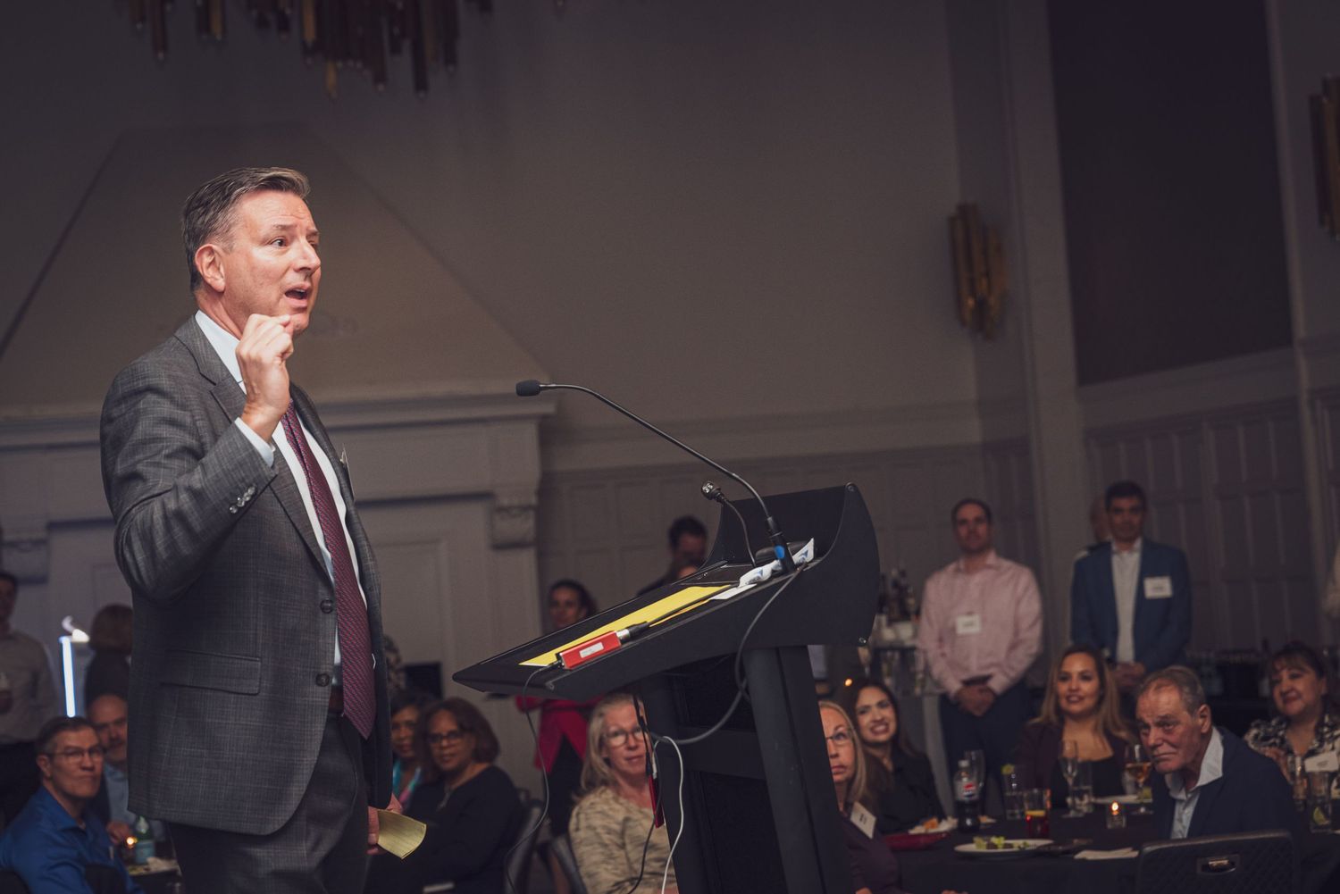 A speaker addresses the audience during a business presentation in a conference room setting.