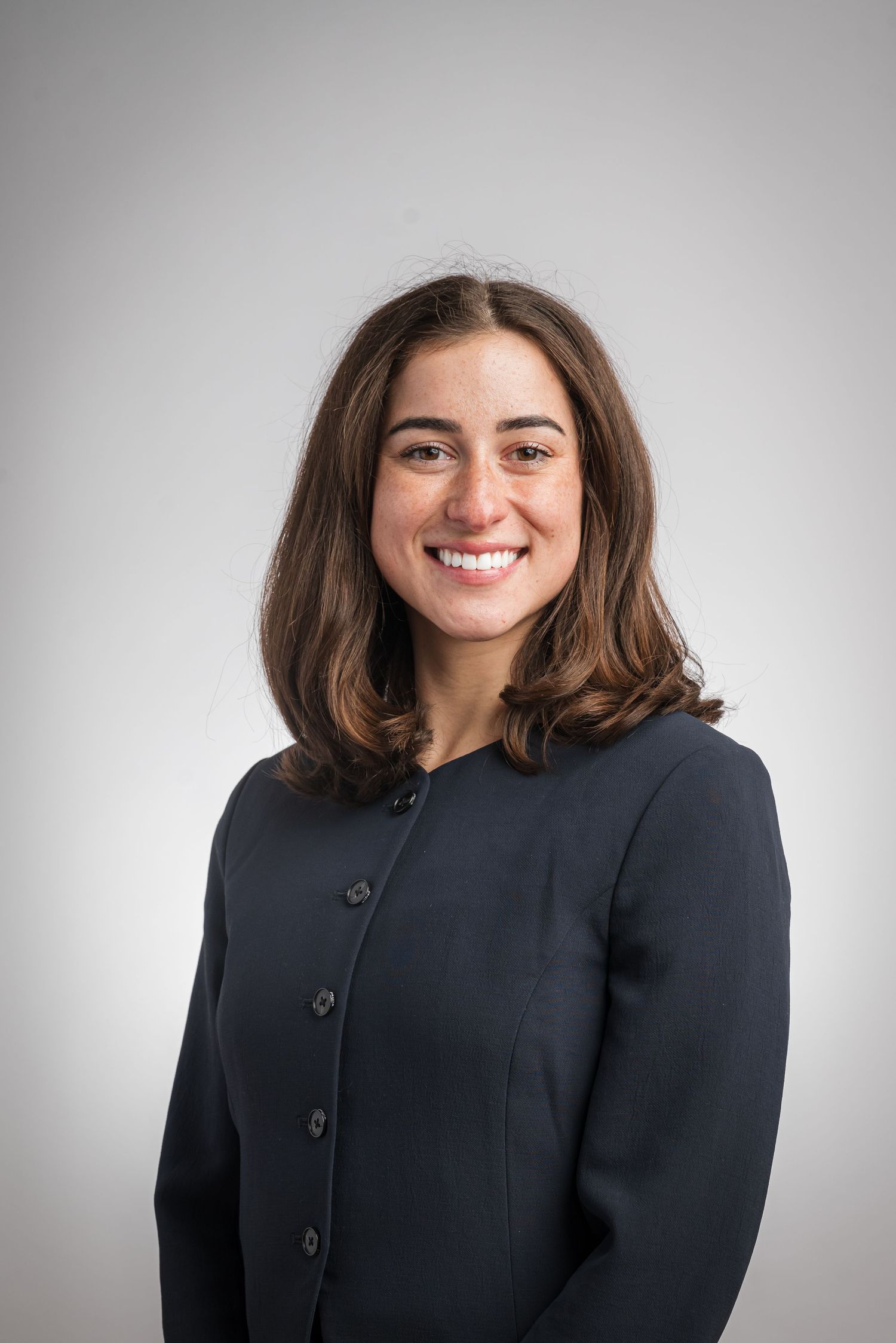Professional headshot of person in dark business attire against gray background.