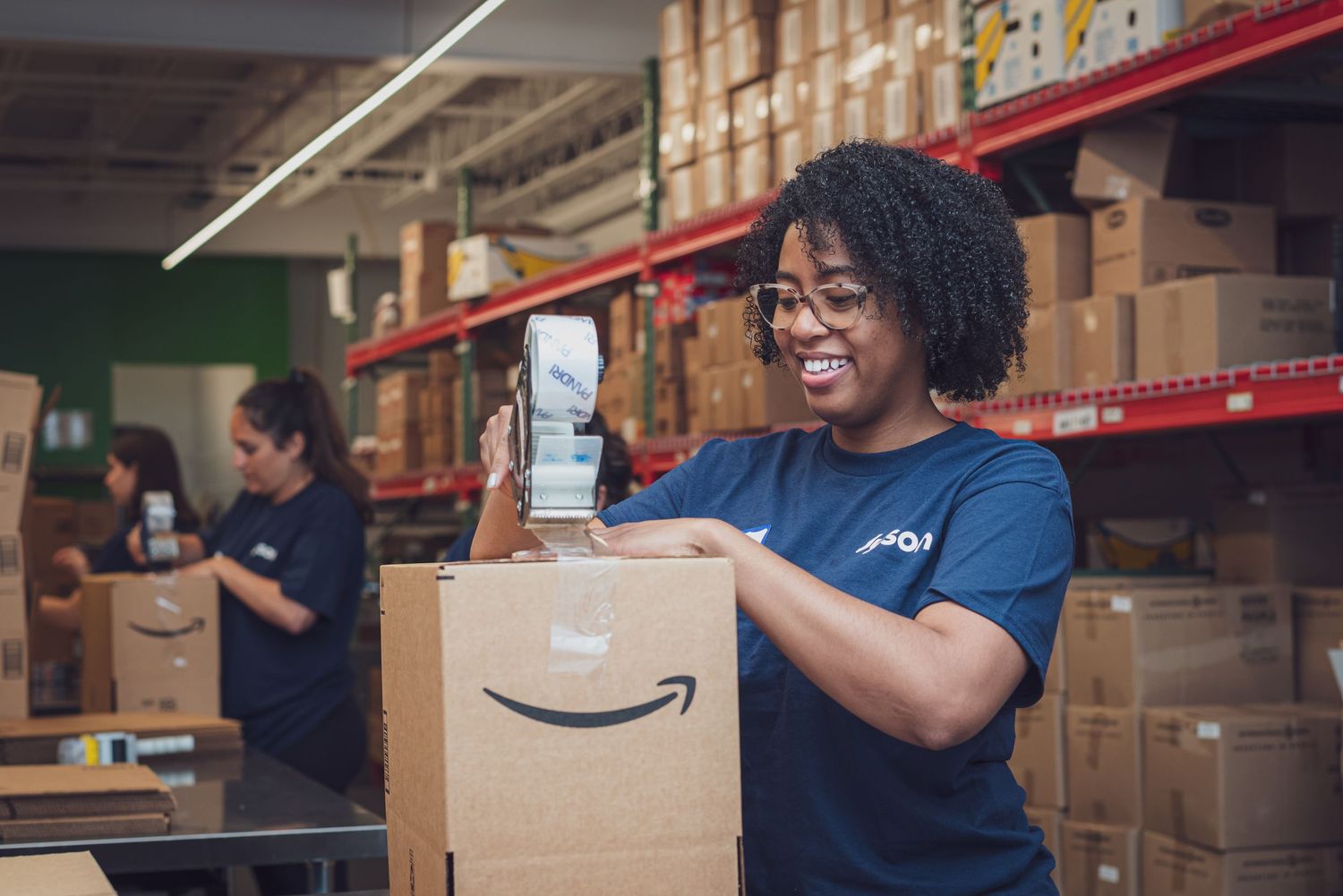 Amazon warehouse worker smiling while holding package in distribution center. goose.img photography LLC - Chicago Photographer