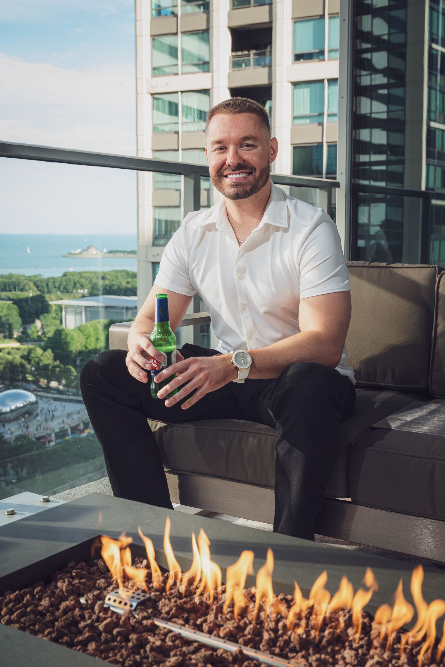 A person relaxes on a modern balcony couch next to a sleek fire feature with city views in the background.