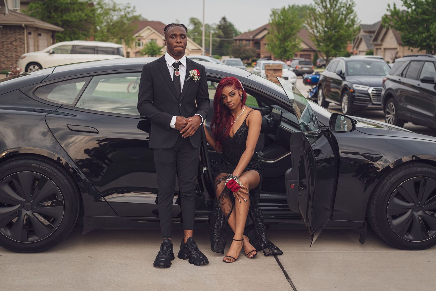 A group of people pose with a black luxury car in a parking lot during a photo shoot.