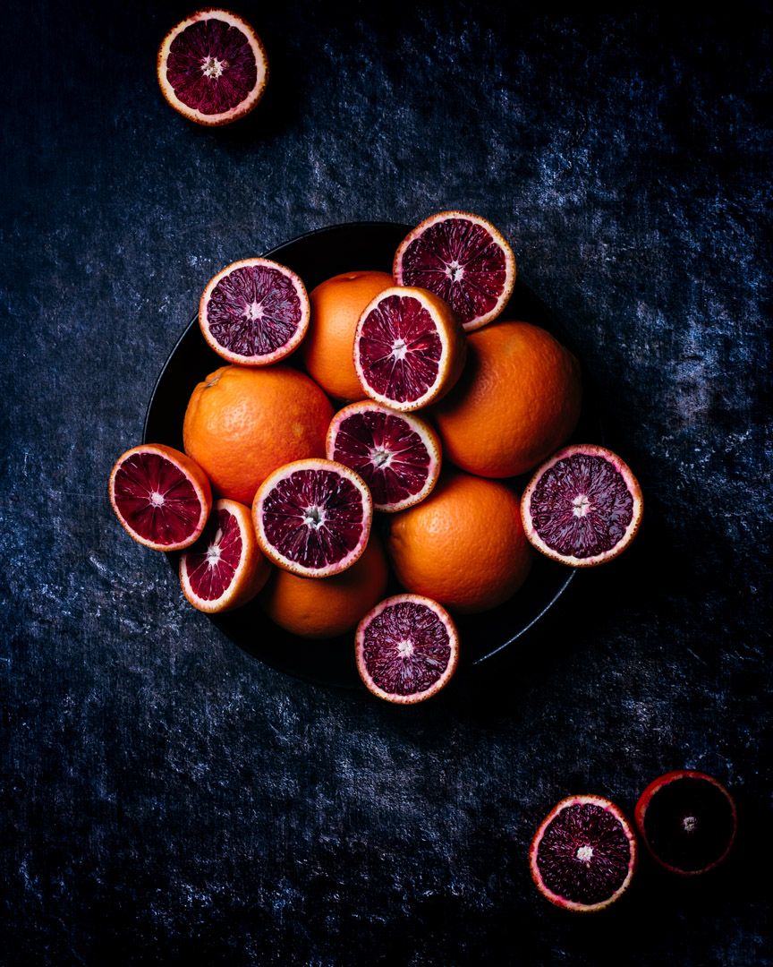 Artistic overhead shot of blood oranges on dark textured surface.