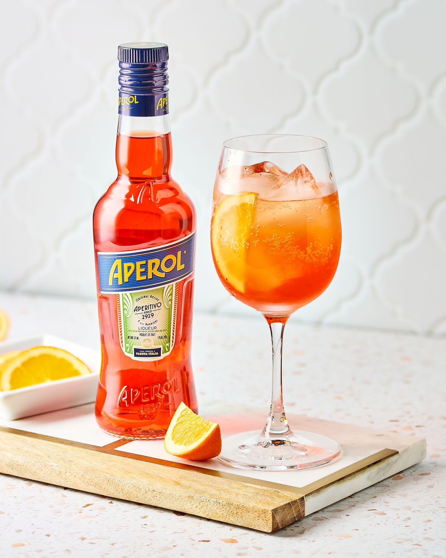Aperol spritz cocktail with orange slice garnish and bottle on wooden board.