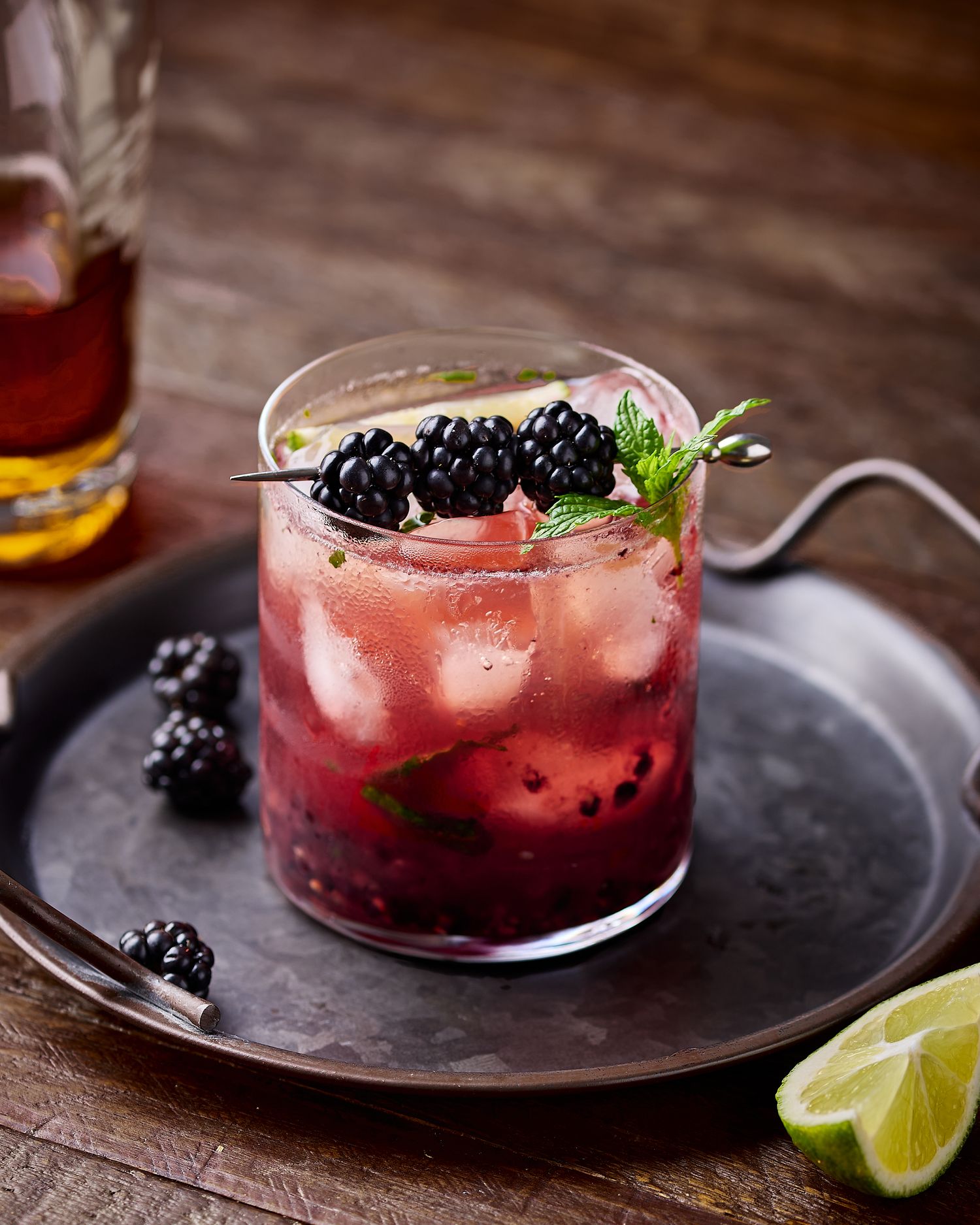 Blackberry cocktail with fresh berries and mint garnish served on a dark plate with lime.