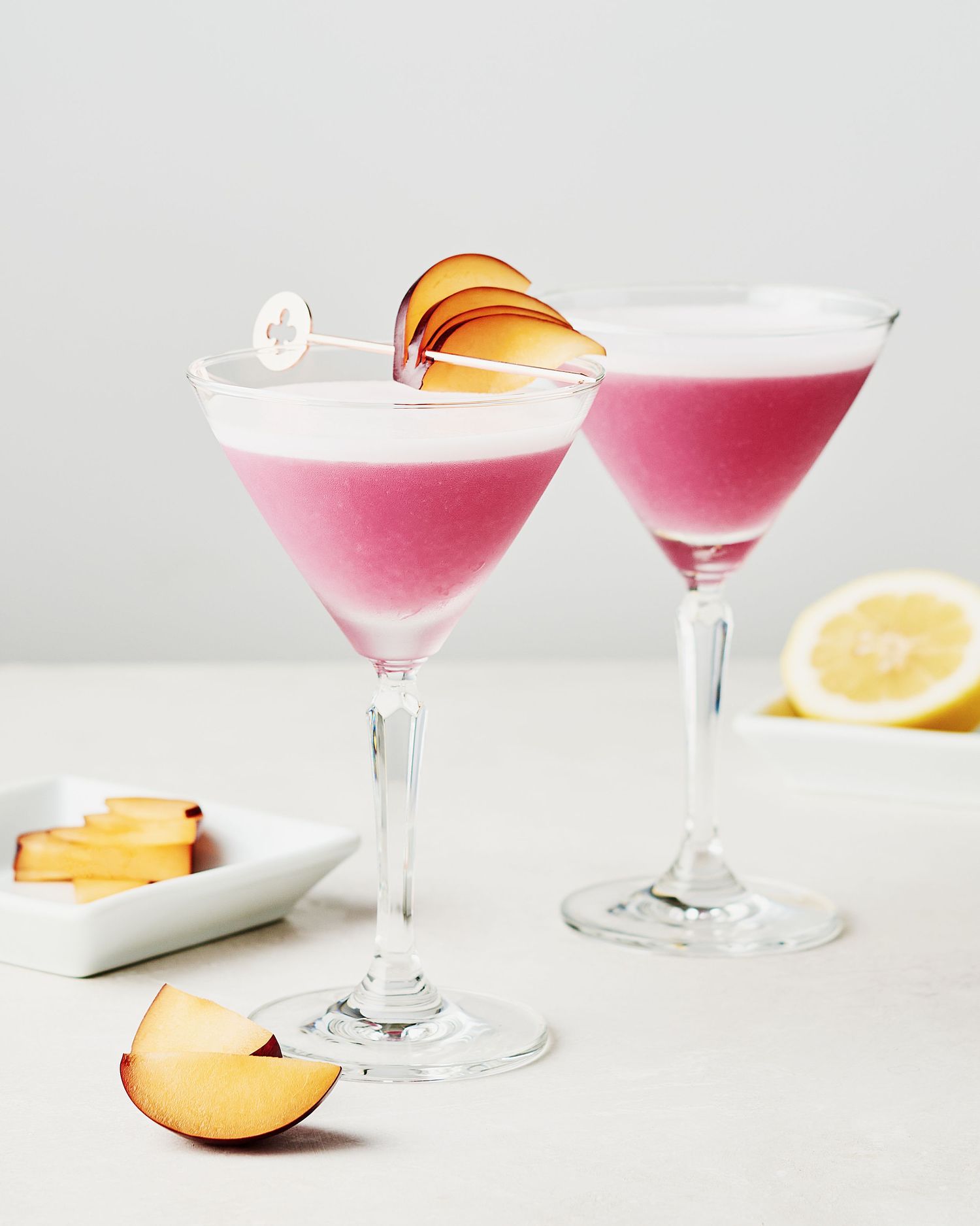 Two pink gin sours garnished with fresh plum slices.