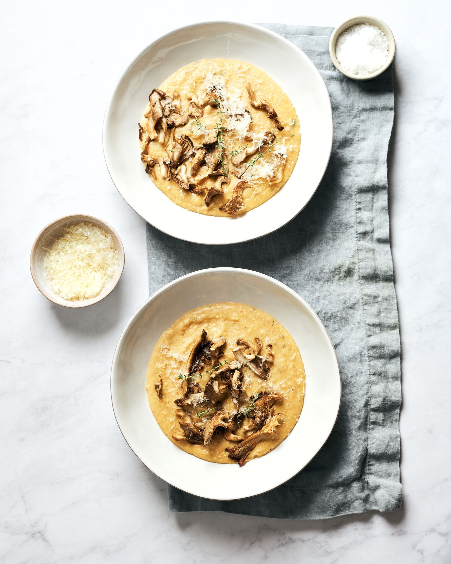 Creamy mushroom polenta served in white bowls with grated vegan parmesan cheese.