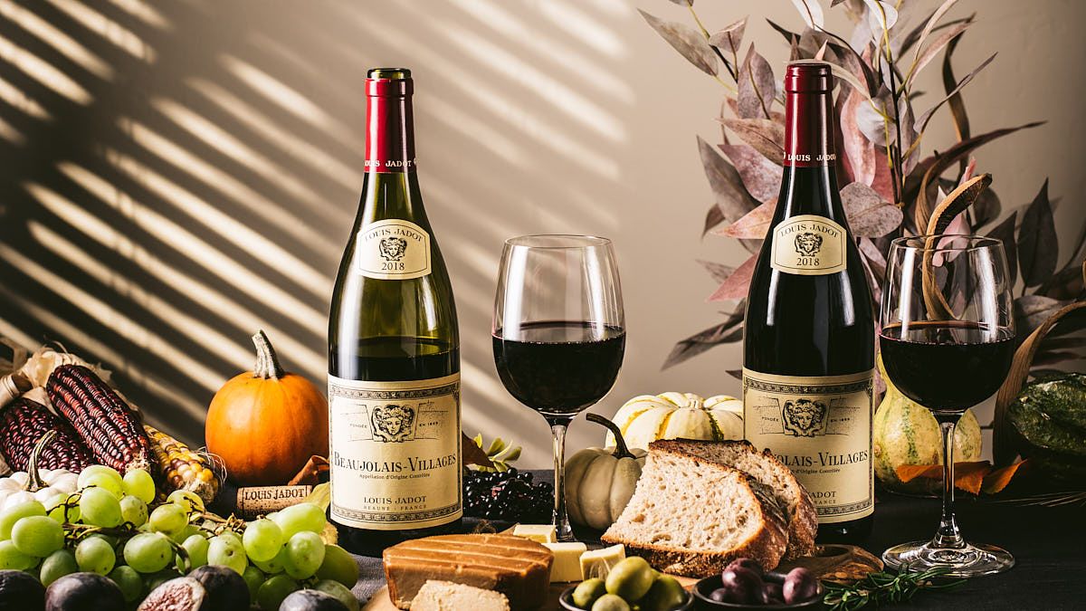 Wine bottles and glasses arranged with autumn decorations and grapes in dramatic lighting.