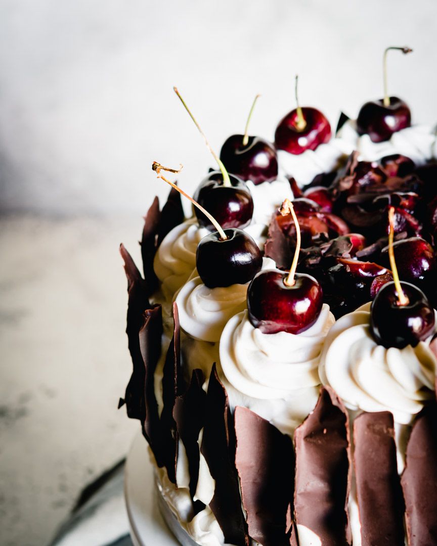 Close-up of chocolate layer cake topped with fresh cherries and dark chocolate shavings.