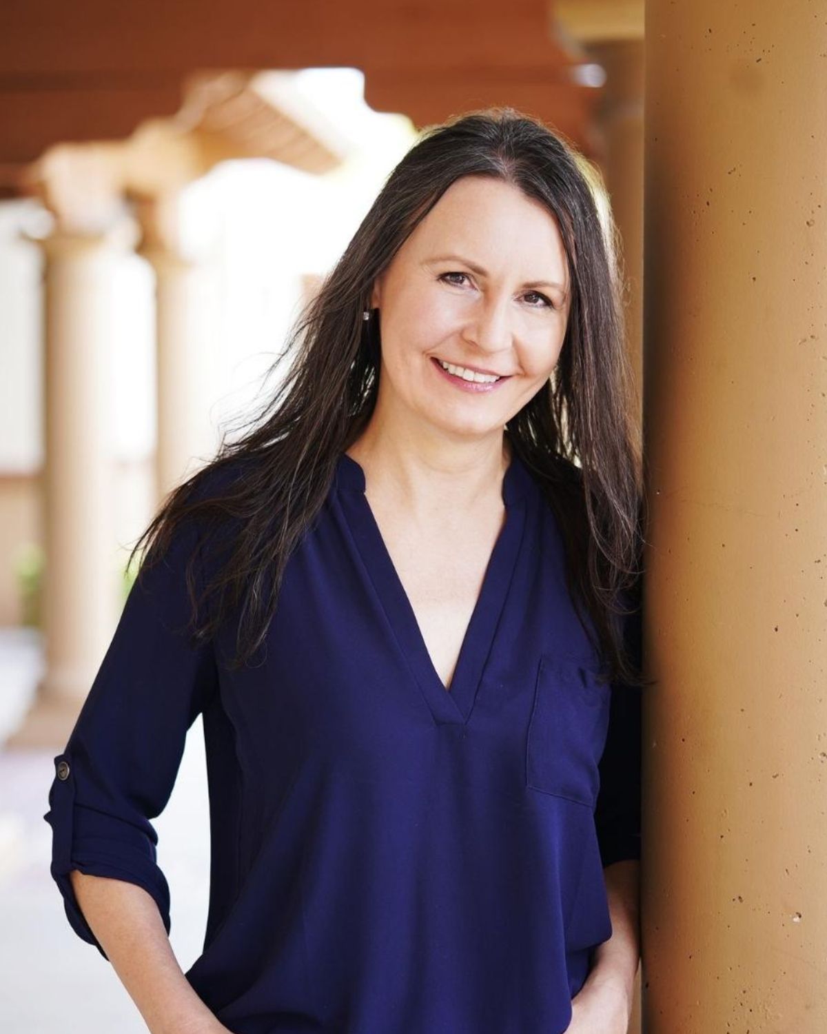 Emily Miller in navy v-neck blouse smiling against architectural columns with warm lighting.