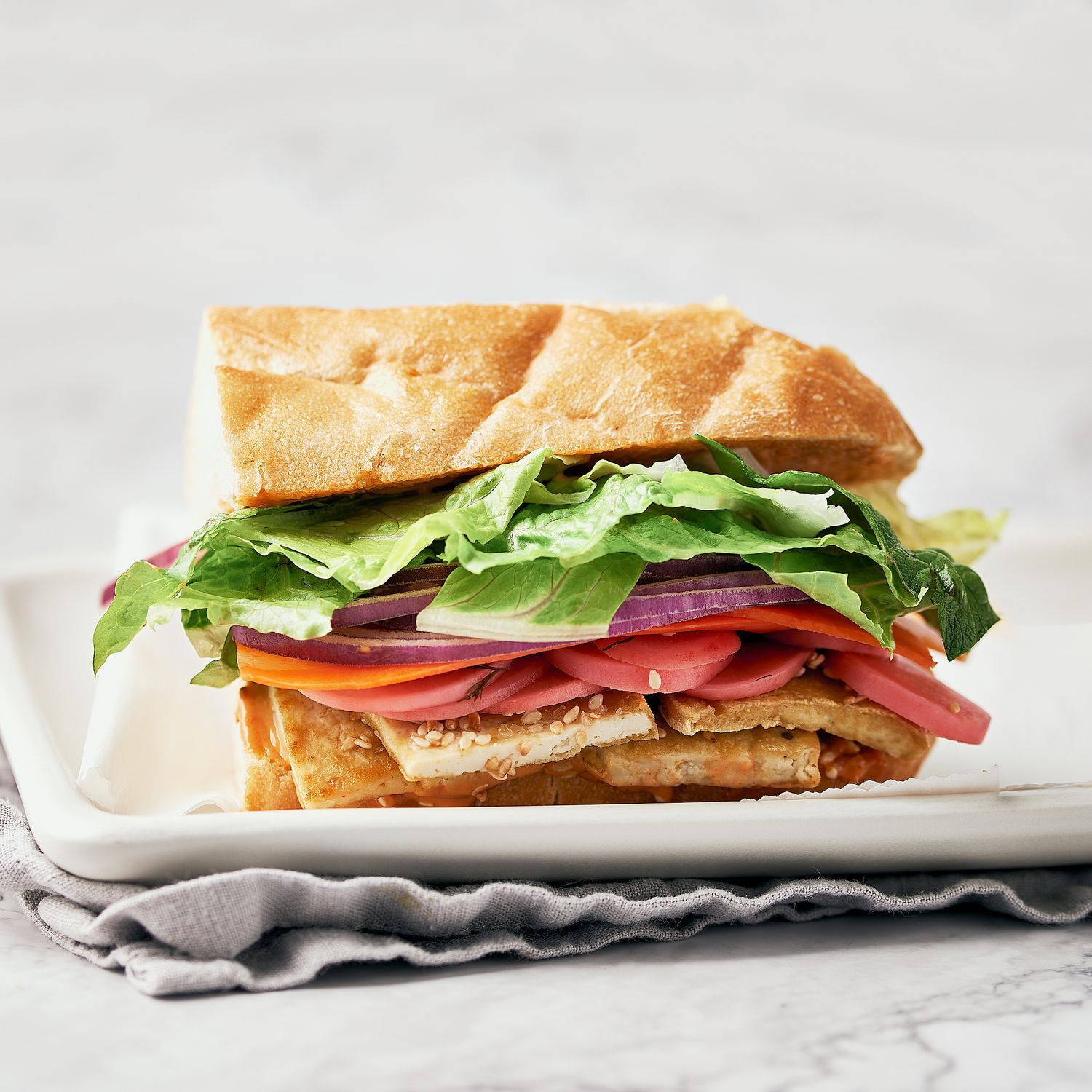 Fresh sandwich filled with lettuce, tomato, and crispy tofu on sliced thick French bread.