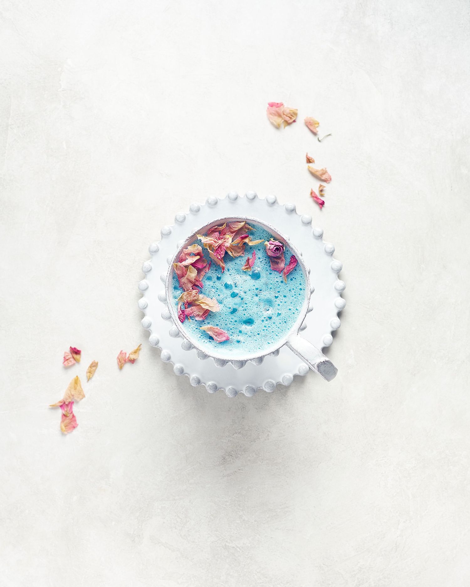 Blue latte in white ceramic cup decorated with dried rose petals.