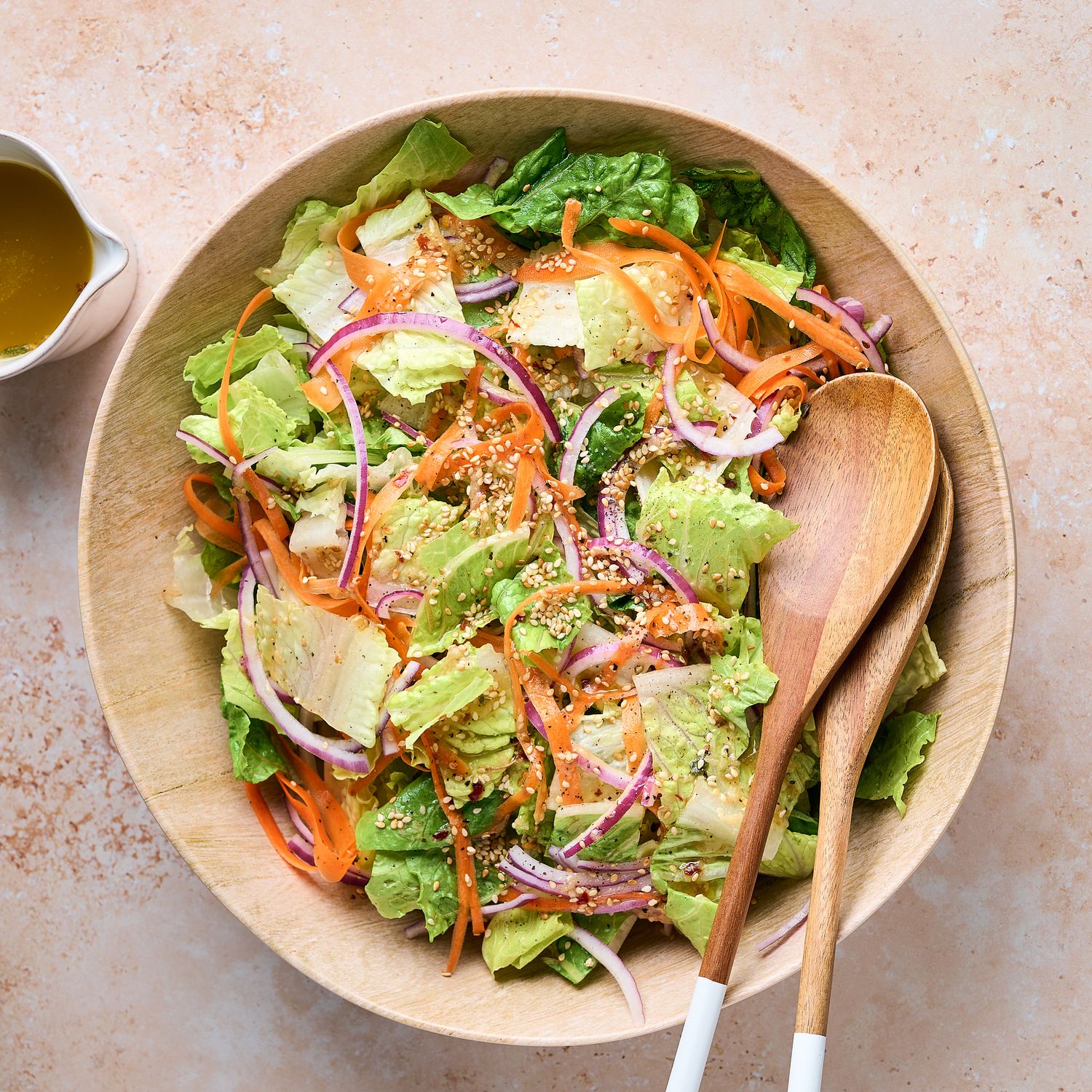 Colorful garden salad with mixed greens, carrots, and red onions in wooden bowl.