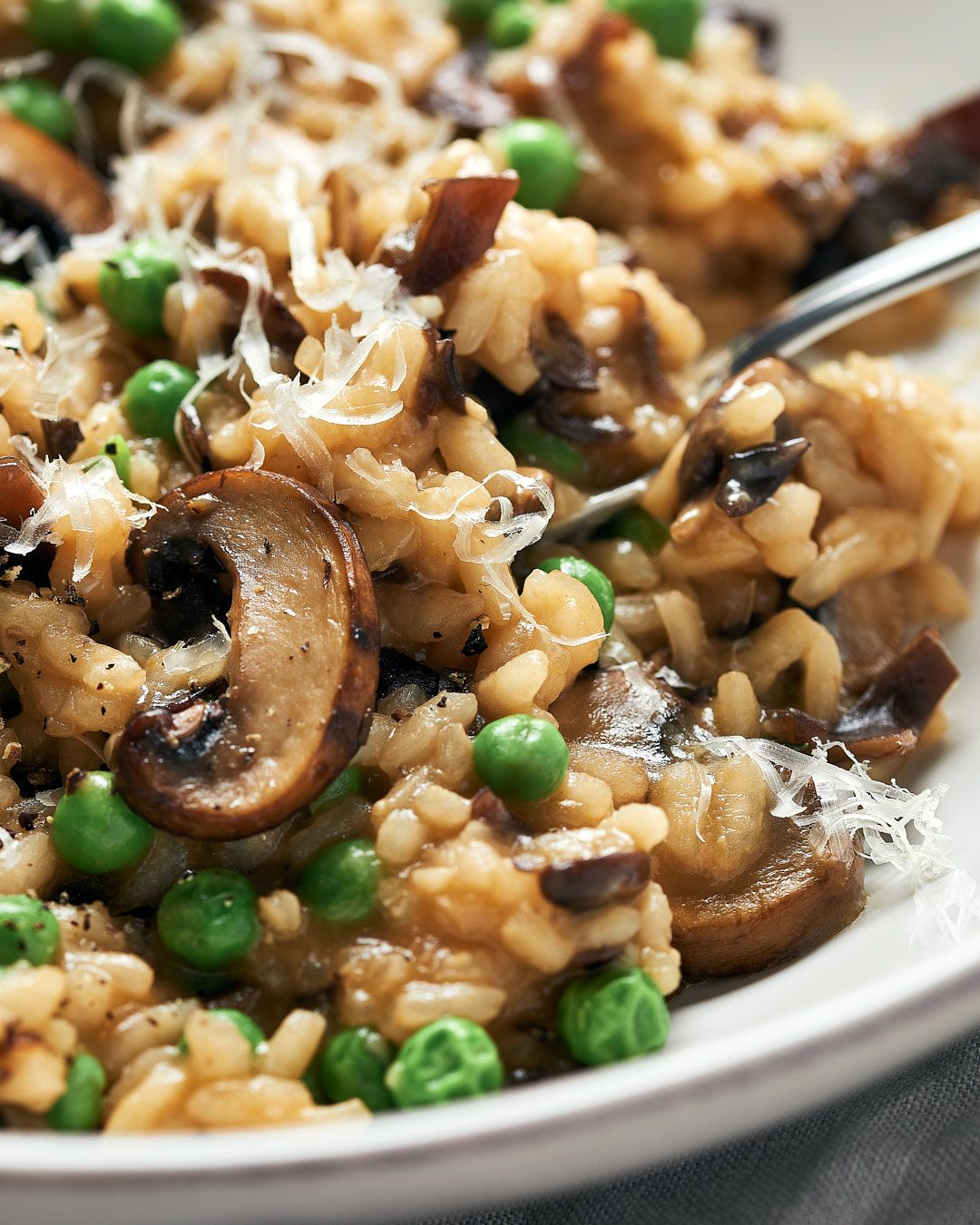 Mushroom and pea risotto garnished with freshly grated vegan parmesan cheese on a white plate.