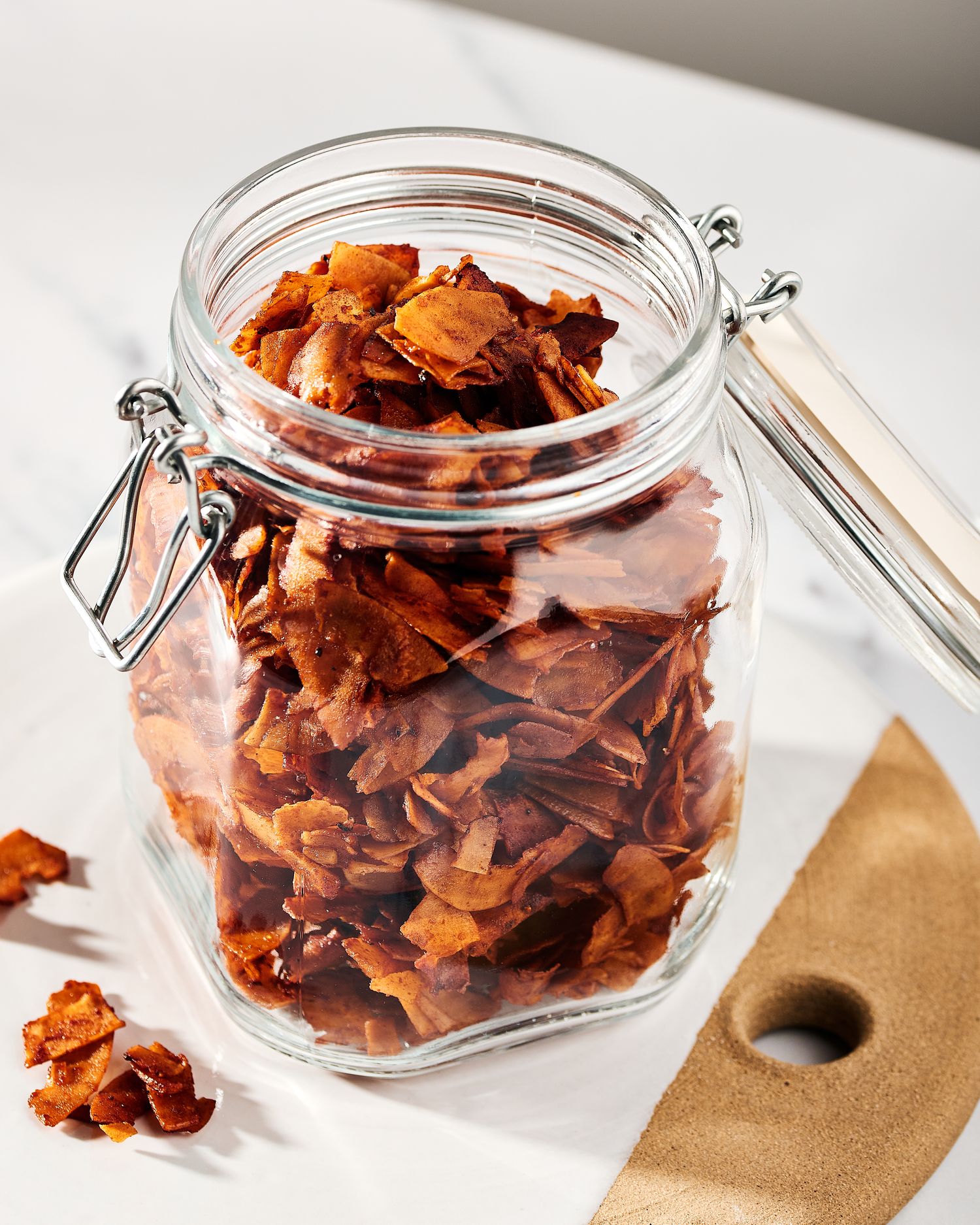 A glass jar filled with homemade crispy vegan bacon bits on white surface.