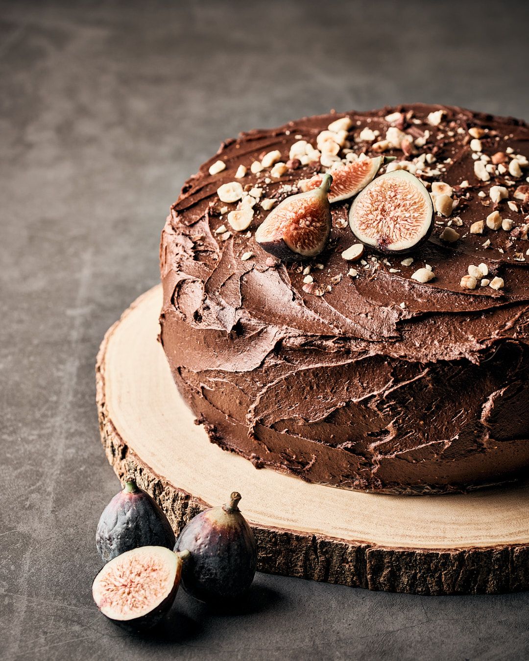Dark chocolate cake topped with fresh figs and chopped nuts on a rustic wooden serving board.