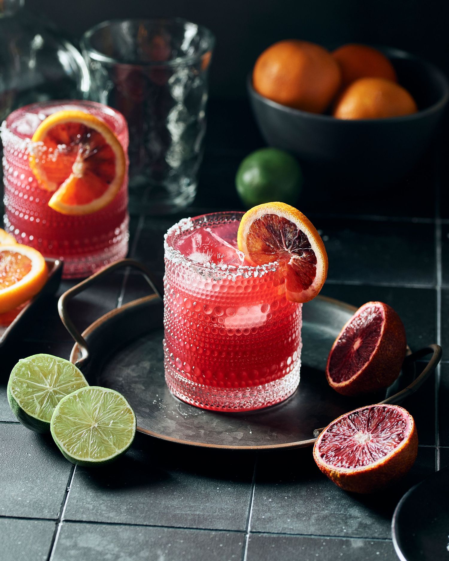 Vibrant red cocktail garnished with blood orange and lime slices in crystal glasses.