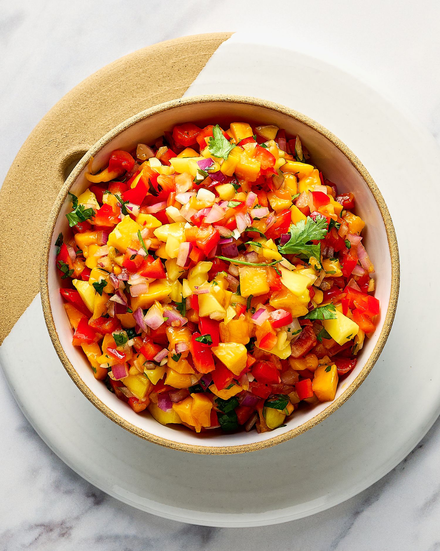 Colorful mango habanero salsa with red peppers, onions, and cilantro in a white bowl.