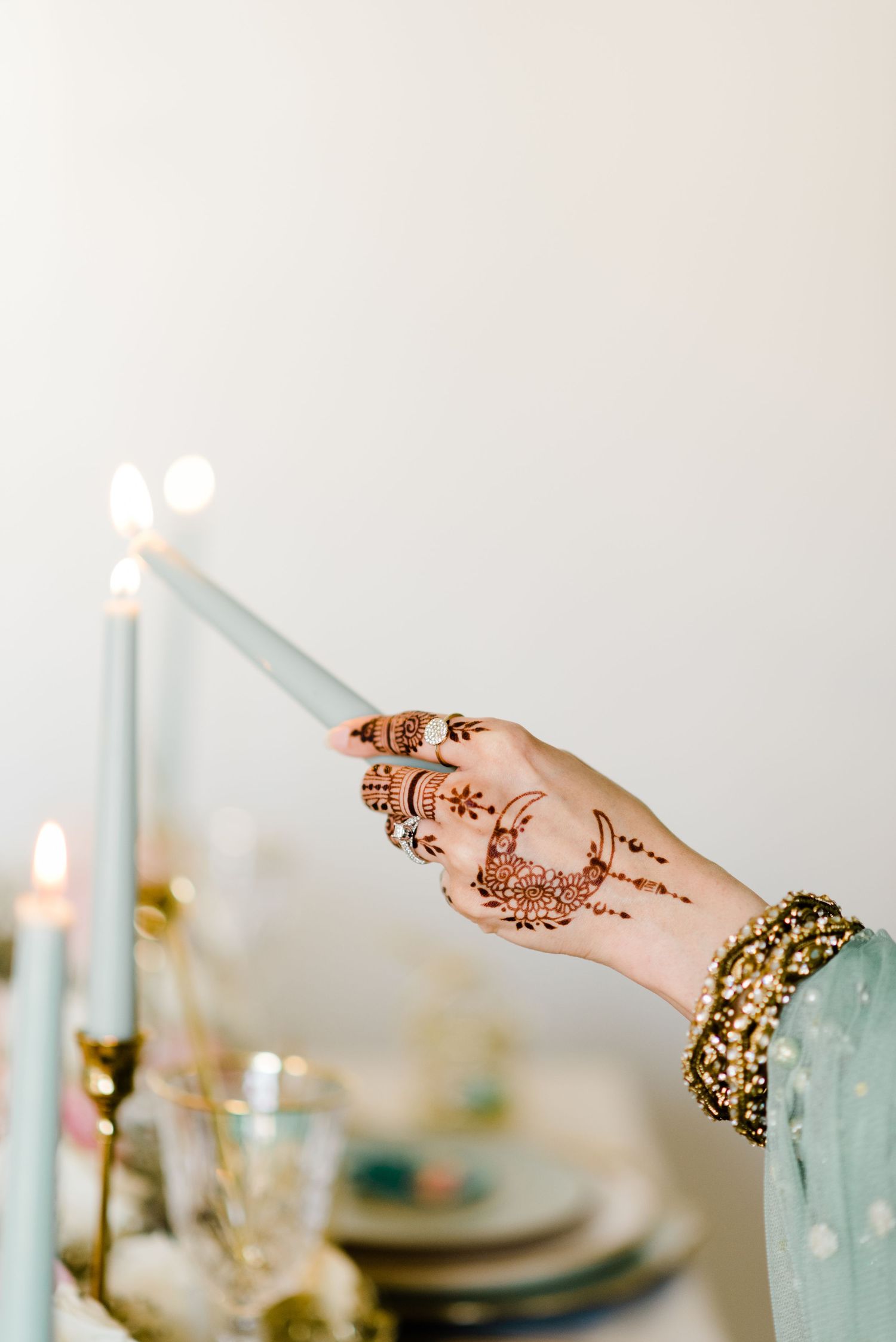 Toronto muslim wedding photographer captures a mehndi bride lighting a blue taper candle, highlighting intricate henna art & shimmering gold