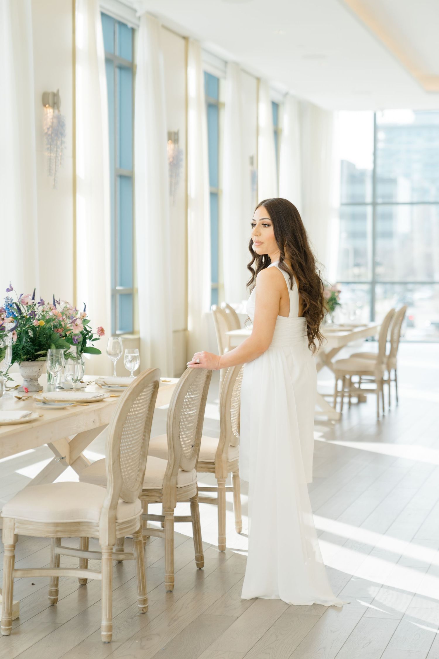 Toronto Muslim wedding photographer captures a bridal shower: bride in a white gown admiring an elegant tablescape bathed in natural light