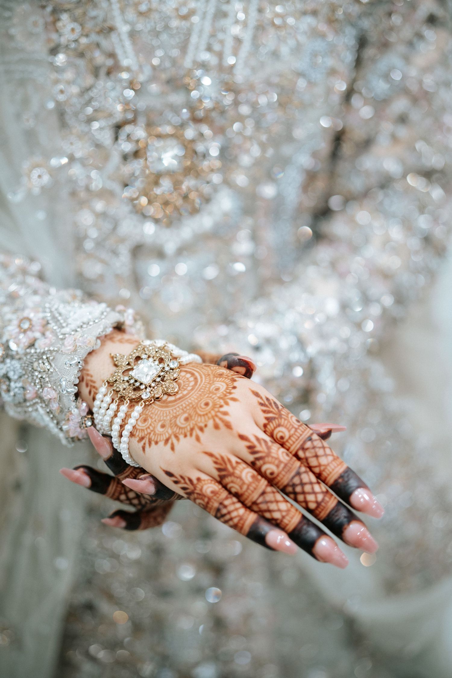 Toronto Pakistani Muslim wedding photographer captures a mehndi bride’s hand with intricate henna, pearl bracelets & shimmering gown.