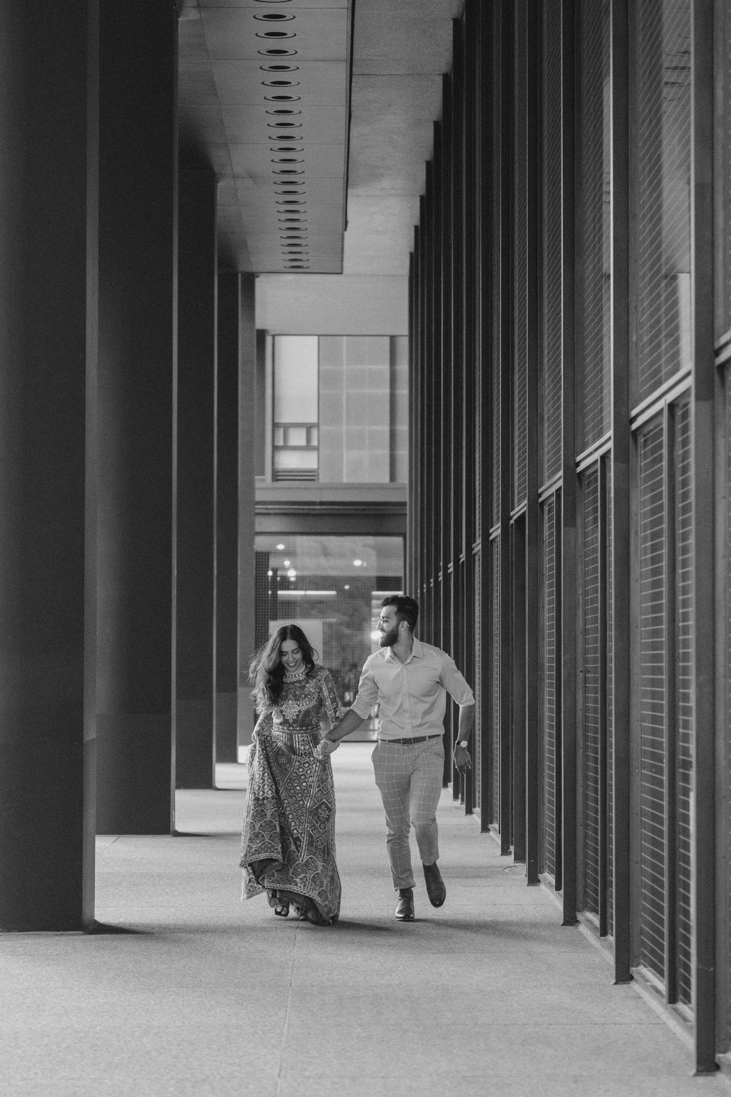 Toronto female wedding photographer captures a Pakistani Muslim couple joyfully hand-in-hand walking through a modern colonnade