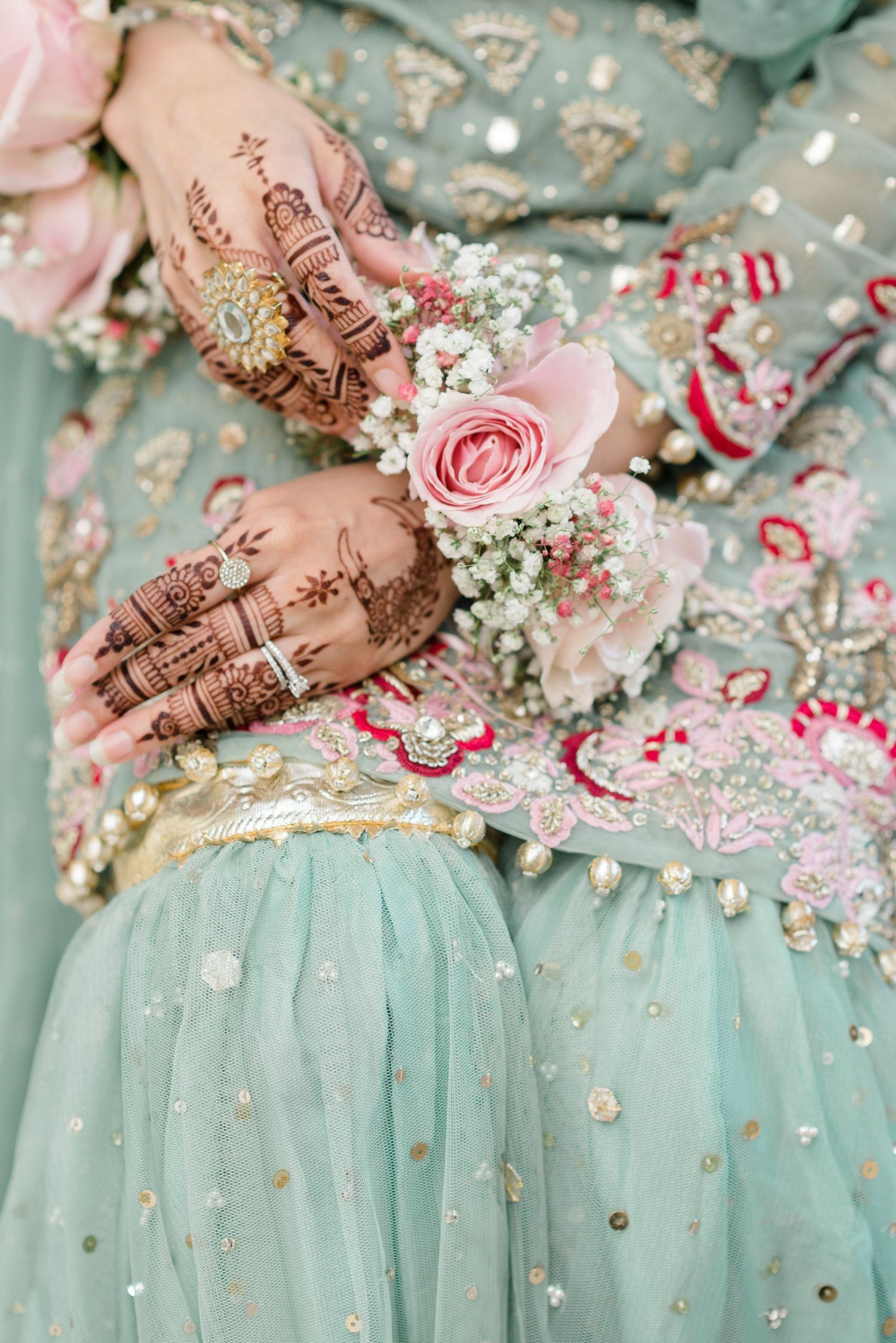Toronto Muslim wedding photographer captures a mehndi bride’s hands holding a pink rose corsage against her pastel mint-green, lehnga