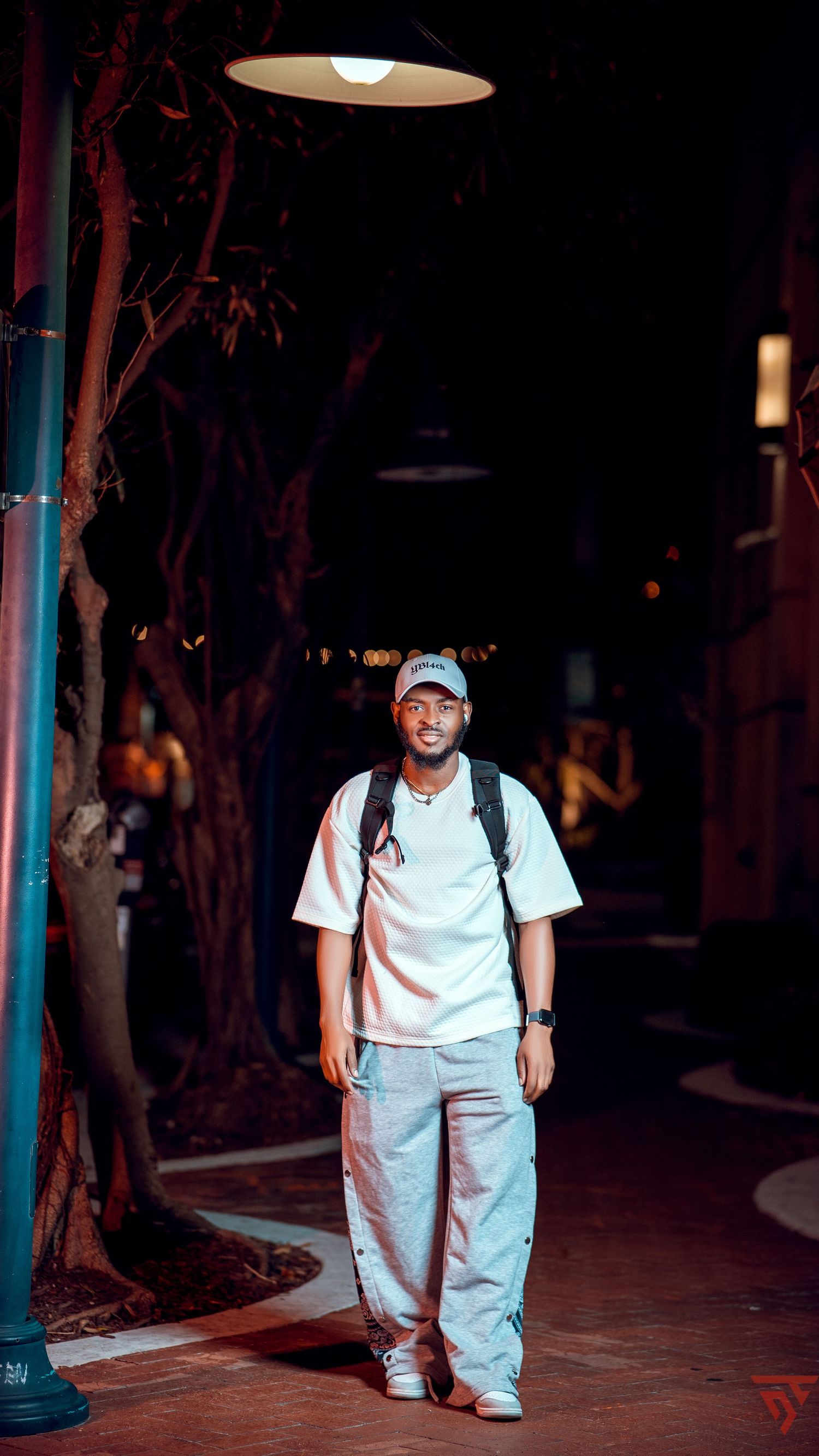 Person in casual white t-shirt and gray pants standing under street lamp at night.