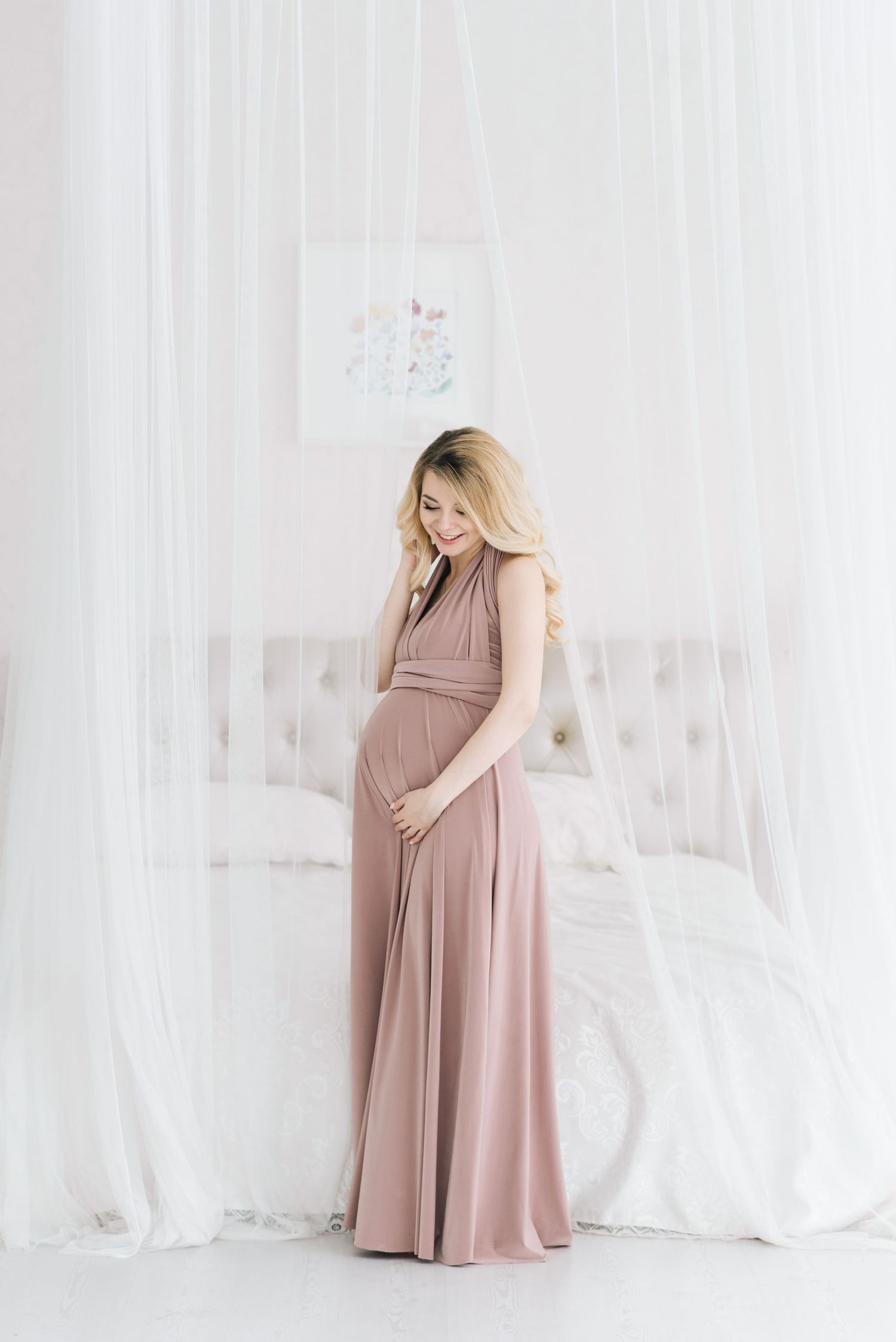 Soft and feminine maternity photos in blush pink dress against white backdrop.