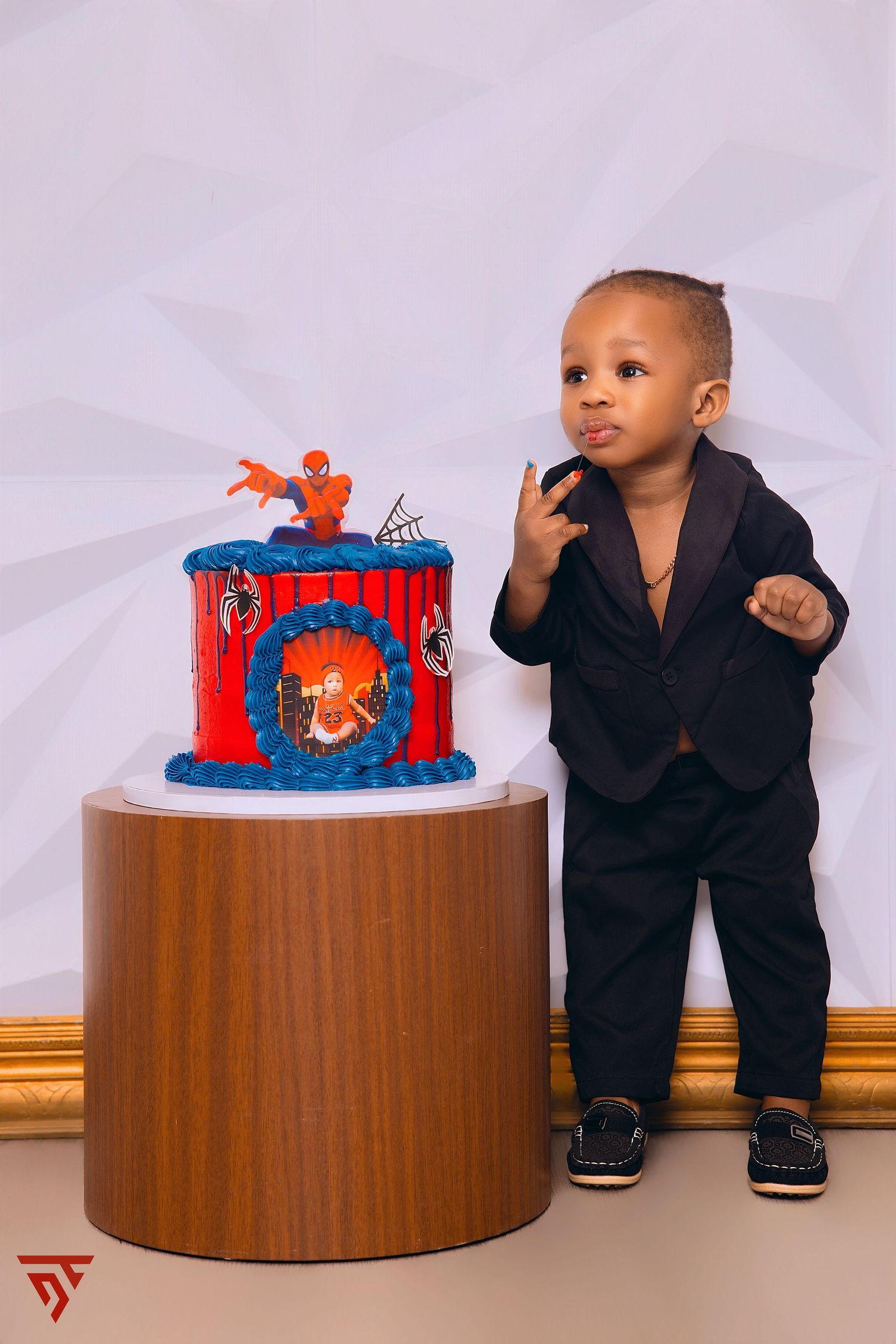 Child in black suit poses with Spider-Man themed birthday cake.